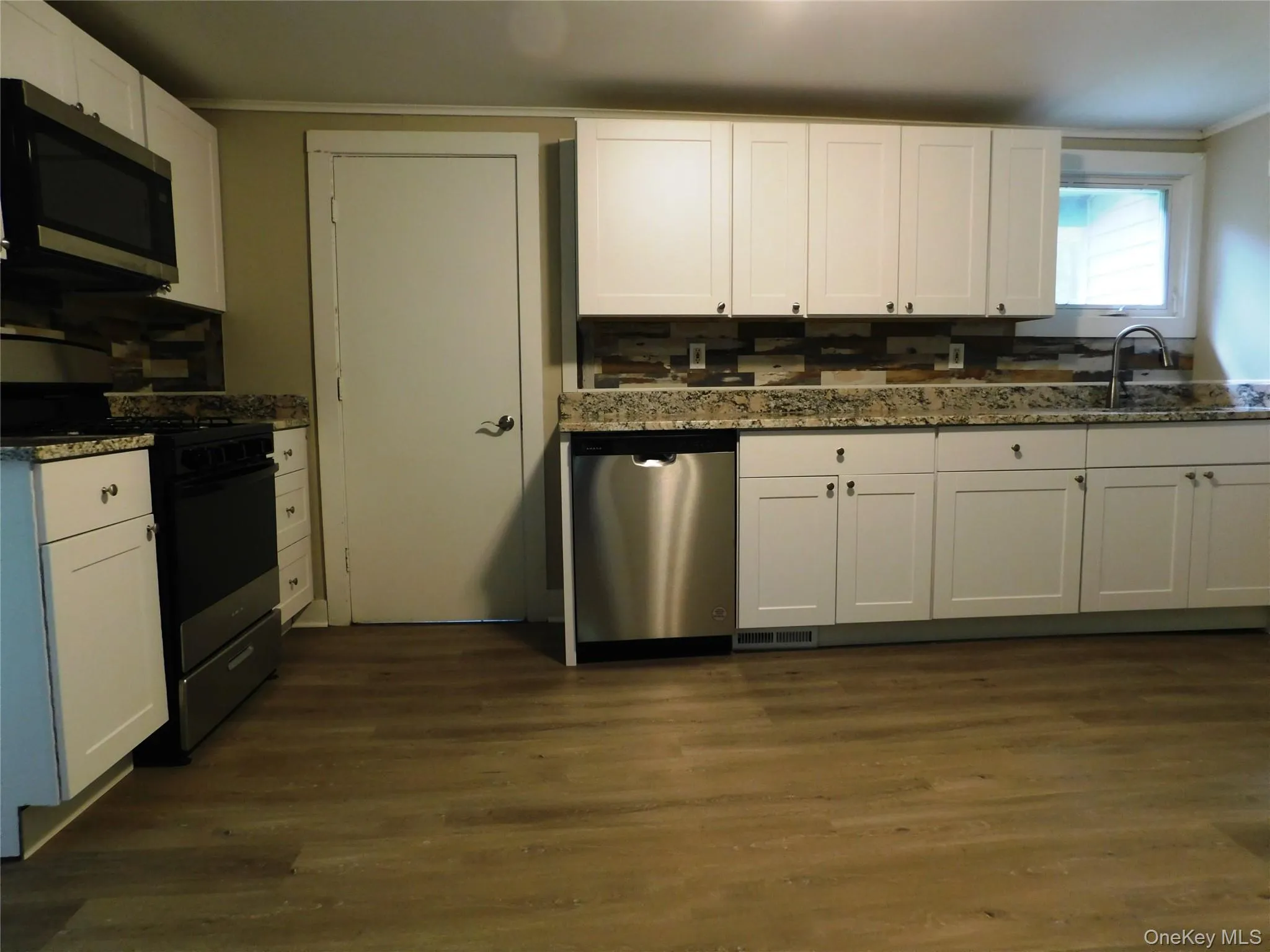 Kitchen featuring wood-finish flooring, white cabinetry, integrated stainless steel appliances, speckled countertops, and a decorative tile backsplash Kitchen featuring wood-finish flooring, white cabinetry, integrated stainless steel appliances, speckled countertops, and a decorative tile backsplash