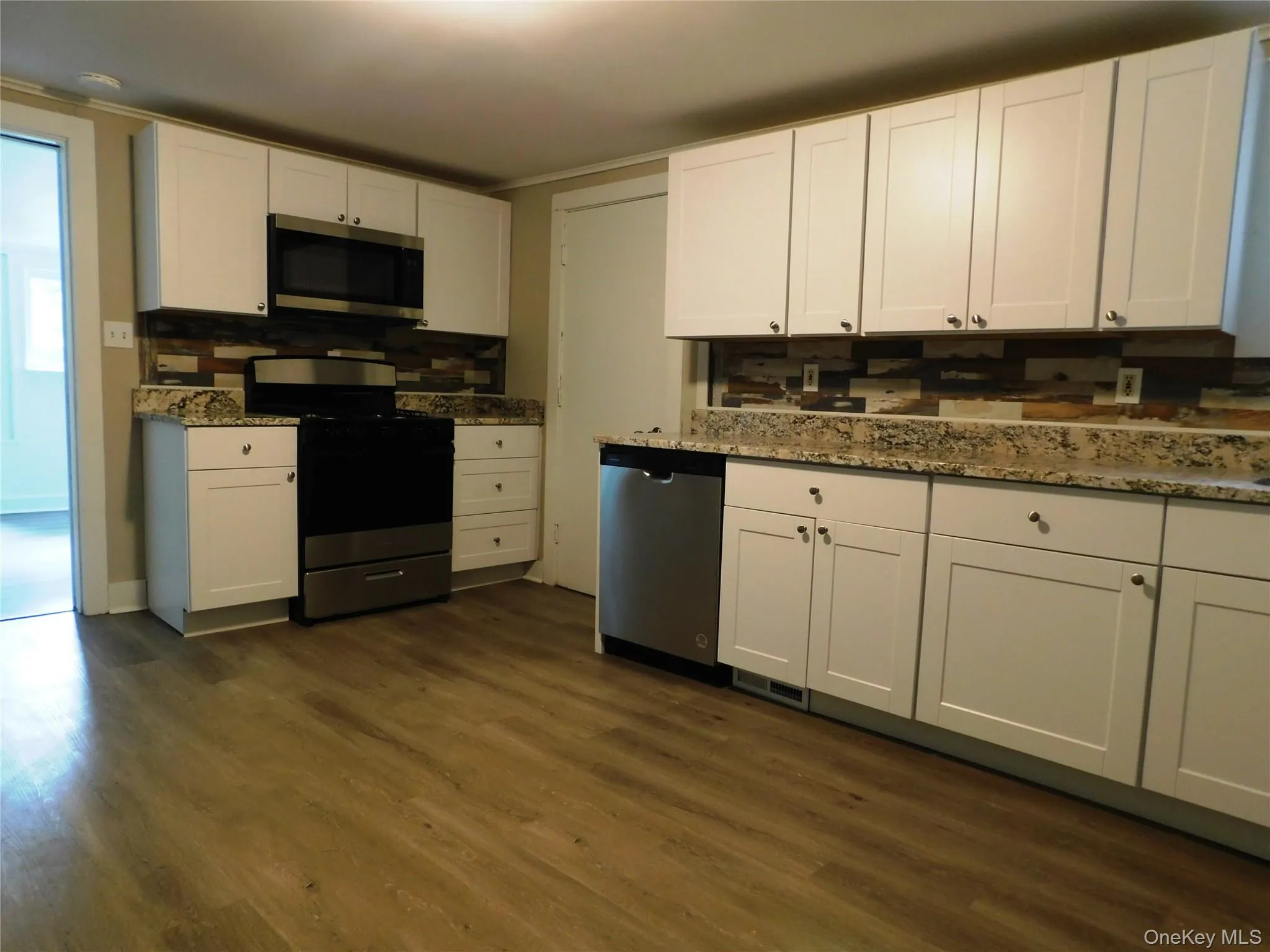 Kitchen featuring white cabinetry, stainless steel appliances, granite-look countertops, and wood-finish flooring Kitchen featuring white cabinetry, stainless steel appliances, granite-look countertops, and wood-finish flooring