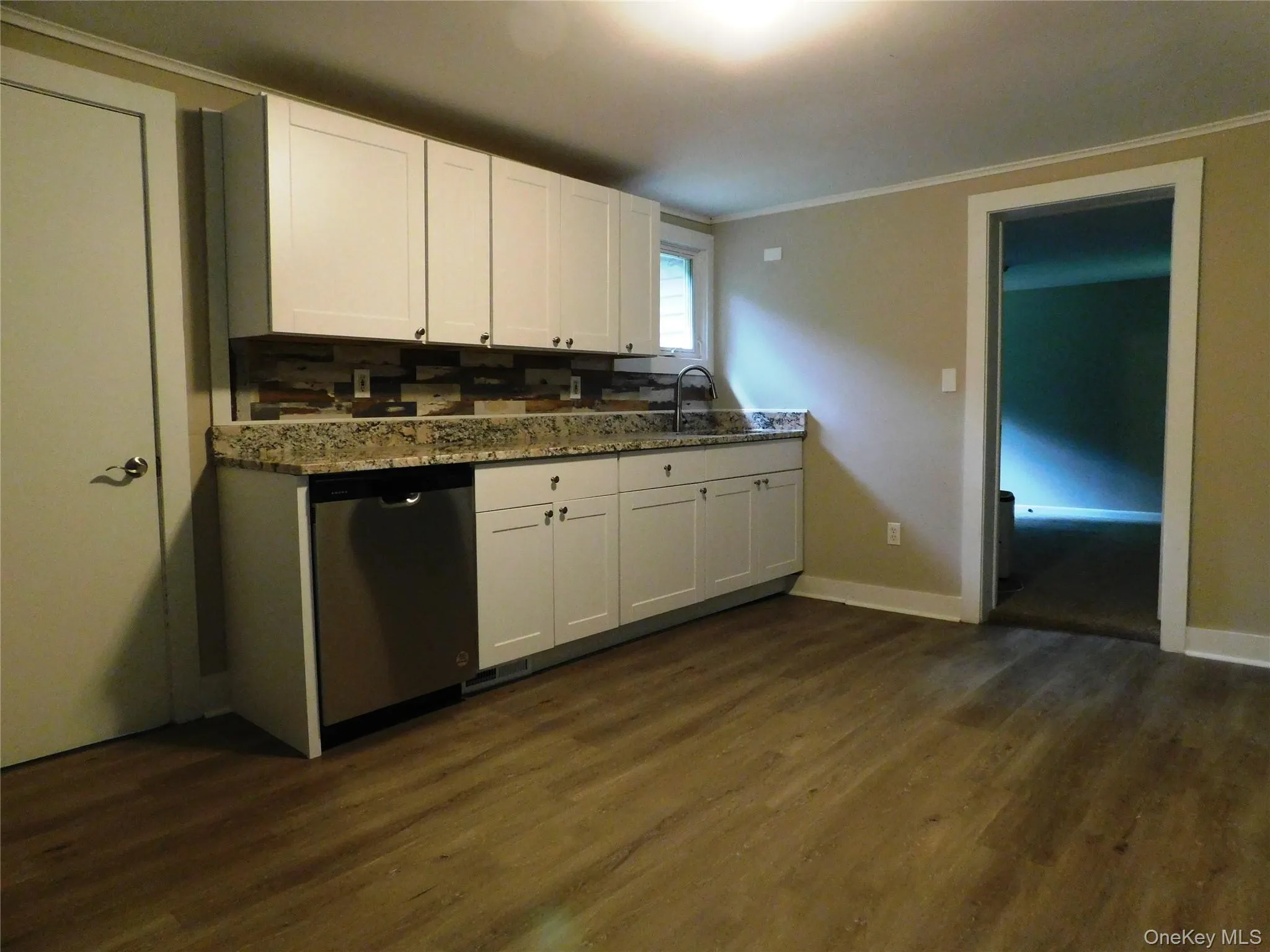 Kitchen featuring wood-finish flooring, white cabinetry, granite-style countertops, a stainless steel dishwasher, and a mosaic tile backsplash Kitchen featuring wood-finish flooring, white cabinetry, granite-style countertops, a stainless steel dishwasher, and a mosaic tile backsplash