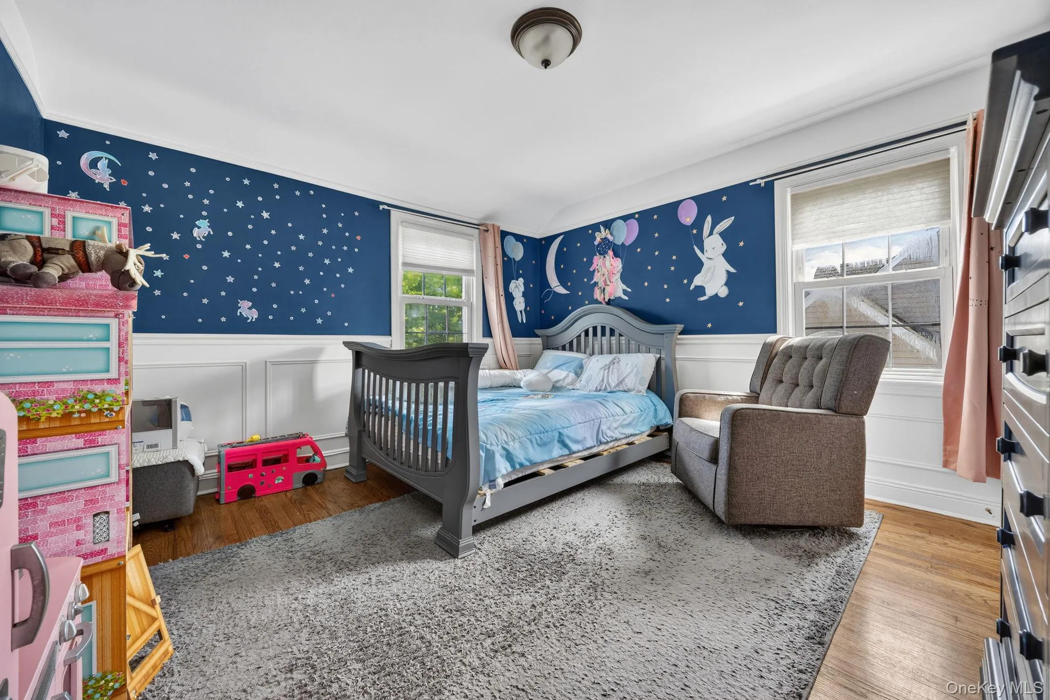 Room featuring hardwood flooring, white wainscoting, and multiple windows with natural light Room featuring hardwood flooring, white wainscoting, and multiple windows with natural light