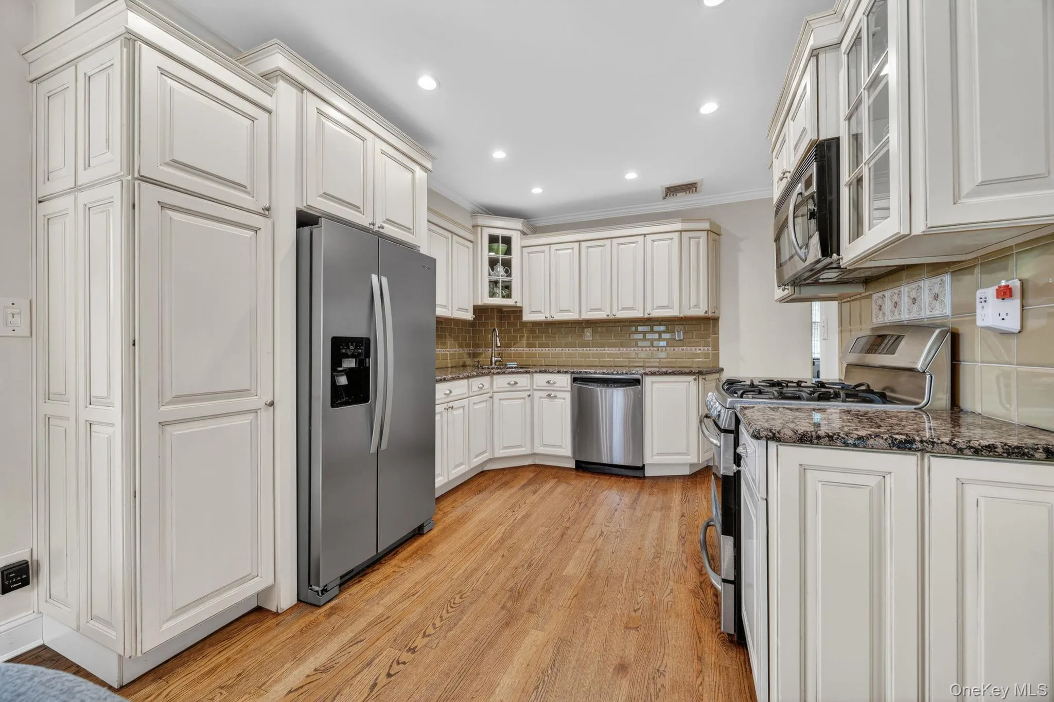 Kitchen featuring light-toned cabinetry, stainless steel appliances, granite countertops, and wood-finish flooring Kitchen featuring light-toned cabinetry, stainless steel appliances, granite countertops, and wood-finish flooring