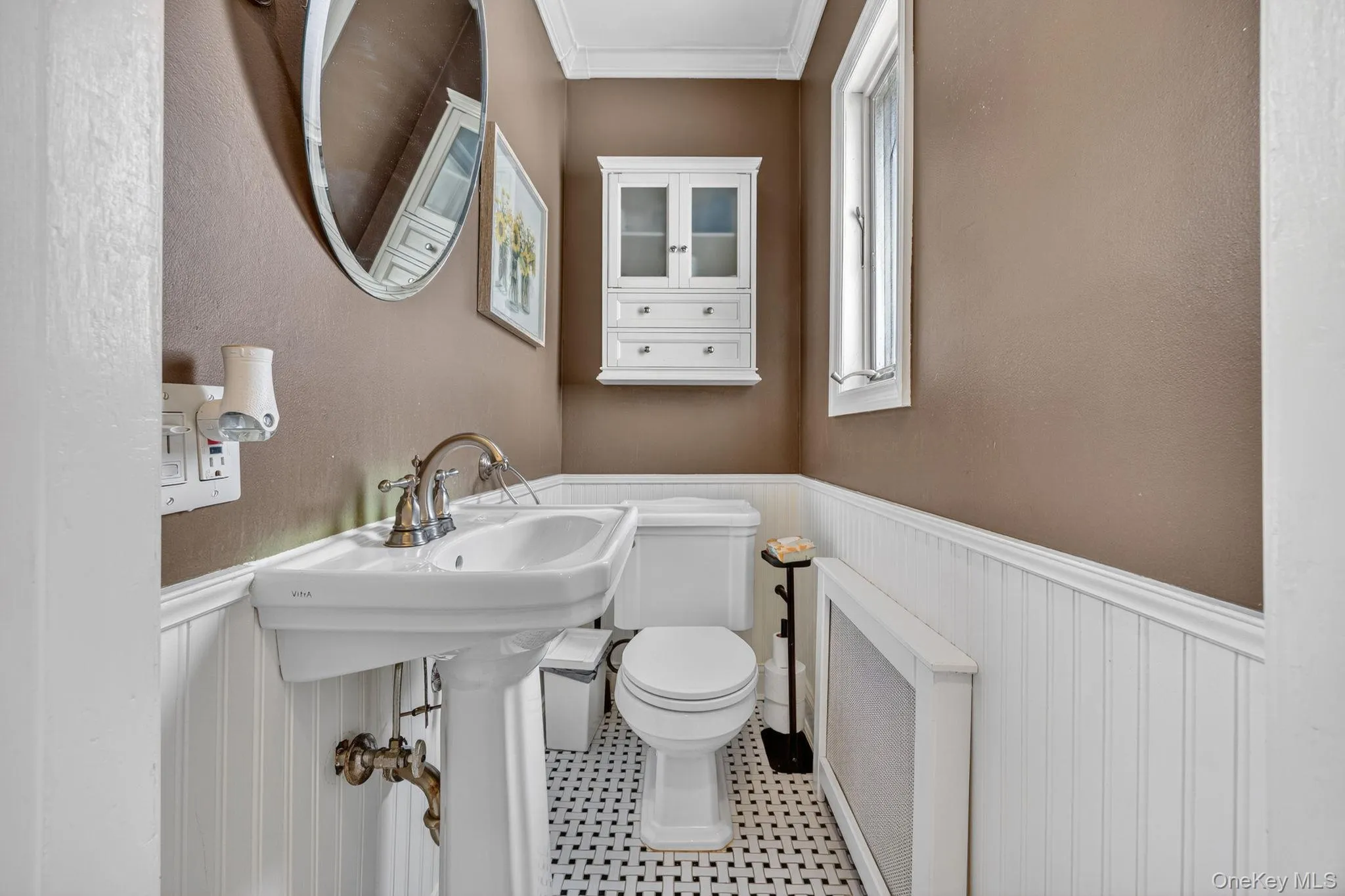 Pedestal sink with brass-finish faucet set, white wainscoting, and a mosaic tile floor Pedestal sink with brass-finish faucet set, white wainscoting, and a mosaic tile floor