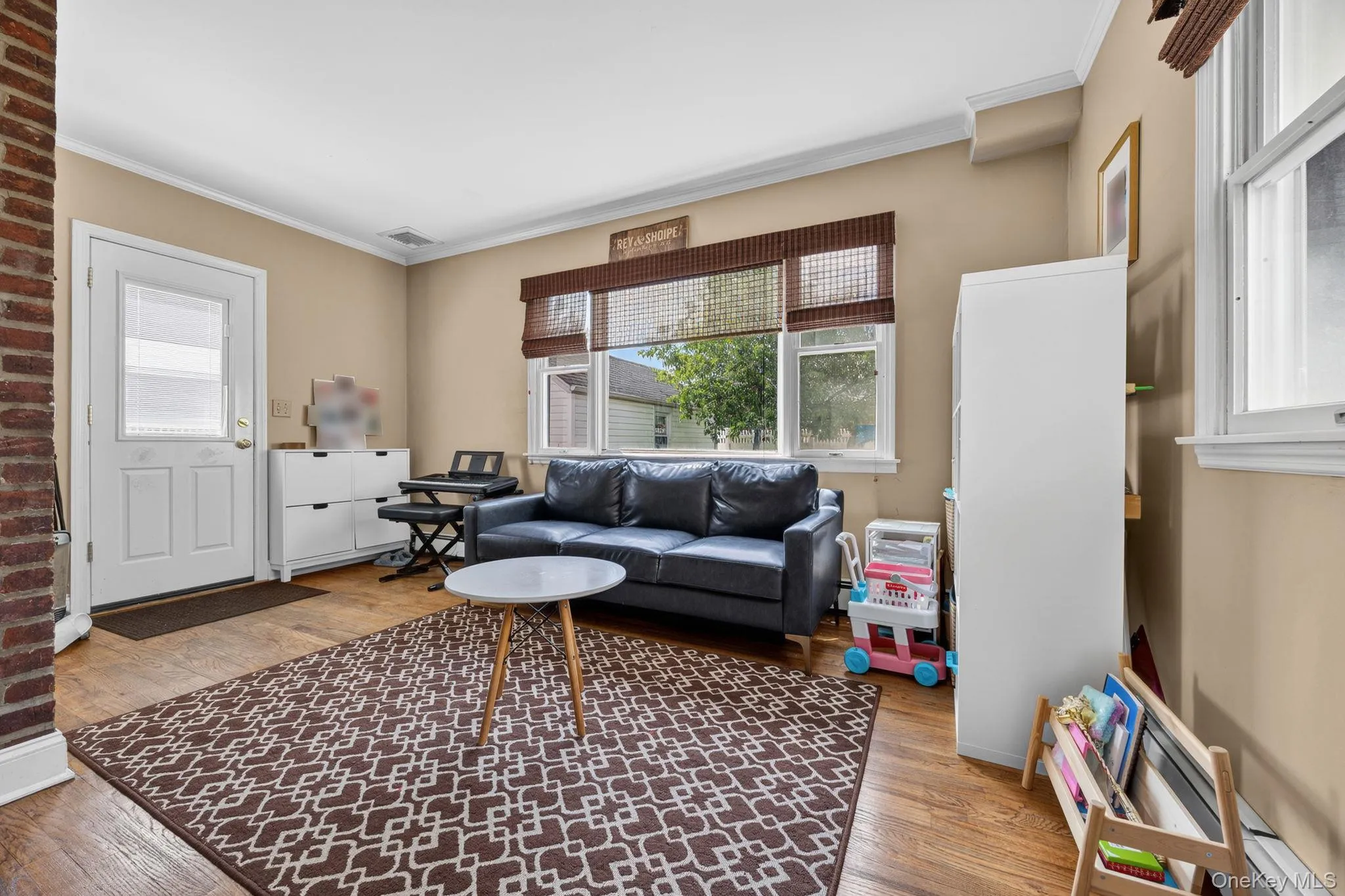 Living area featuring wood-finish flooring, a white paneled entry door with frosted glass, and crown molding Living area featuring wood-finish flooring, a white paneled entry door with frosted glass, and crown molding