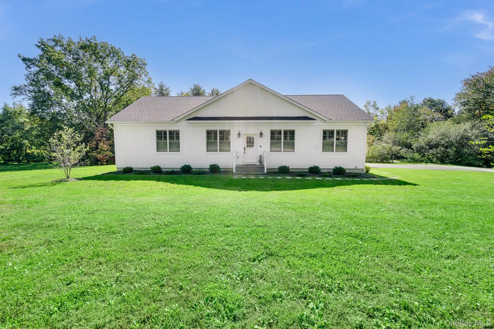 White-sided single-story home featuring a central gable and dark-shingle roofing White-sided single-story home featuring a central gable and dark-shingle roofing