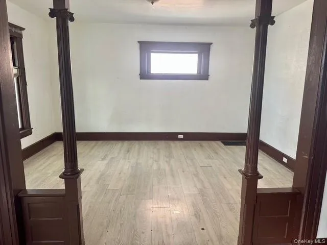Spacious interior room featuring wood-finish flooring, white walls, and dark wood trim Spacious interior room featuring wood-finish flooring, white walls, and dark wood trim