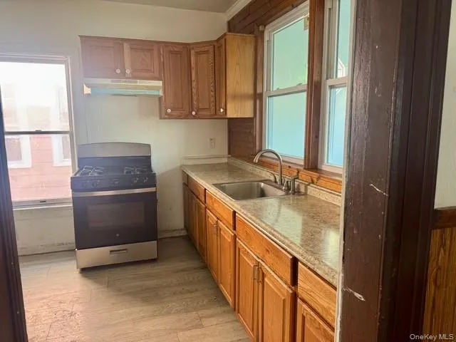 Kitchen featuring wood-finish cabinetry, light-toned countertops, and a stainless steel gas range with an overhead vent Kitchen featuring wood-finish cabinetry, light-toned countertops, and a stainless steel gas range with an overhead vent