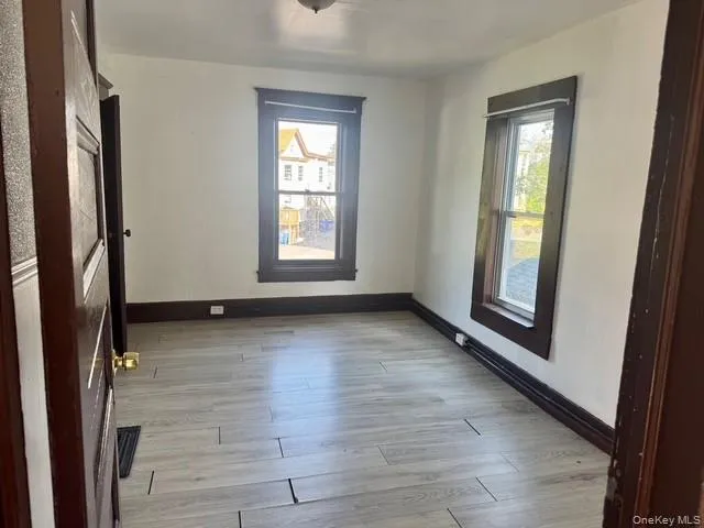 Room featuring wood-finish flooring, two window openings with dark trim, and white painted walls Room featuring wood-finish flooring, two window openings with dark trim, and white painted walls