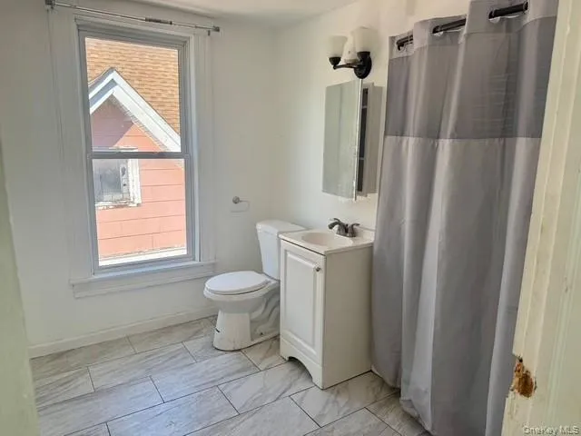 Bathroom featuring tile flooring, single vanity with integrated sink, wall-mounted medicine cabinet, toilet, and shower with curtain rod Bathroom featuring tile flooring, single vanity with integrated sink, wall-mounted medicine cabinet, toilet, and shower with curtain rod