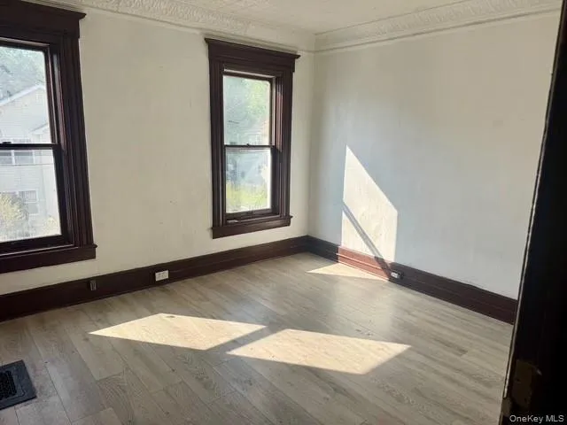 Room featuring two windows with dark trim, wood-finish flooring, and white walls Room featuring two windows with dark trim, wood-finish flooring, and white walls