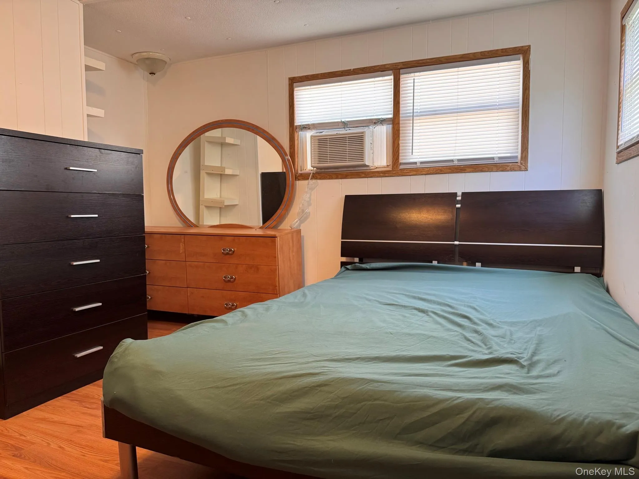 Room featuring wood-finish flooring, two windows with blinds, and white panel walls Room featuring wood-finish flooring, two windows with blinds, and white panel walls