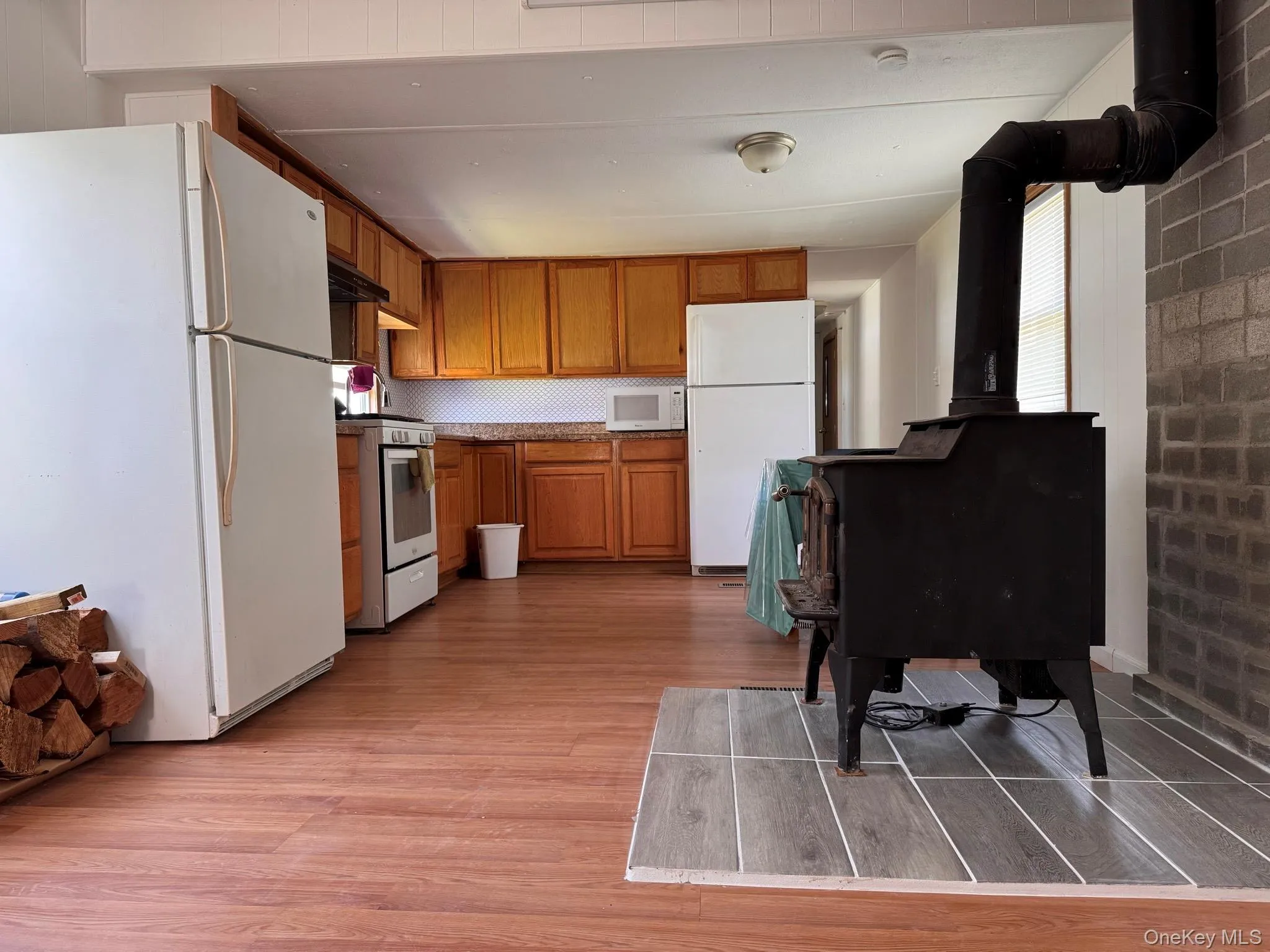 Kitchen featuring wood-finish flooring, wood cabinetry, white appliances, and a tile backsplash Kitchen featuring wood-finish flooring, wood cabinetry, white appliances, and a tile backsplash