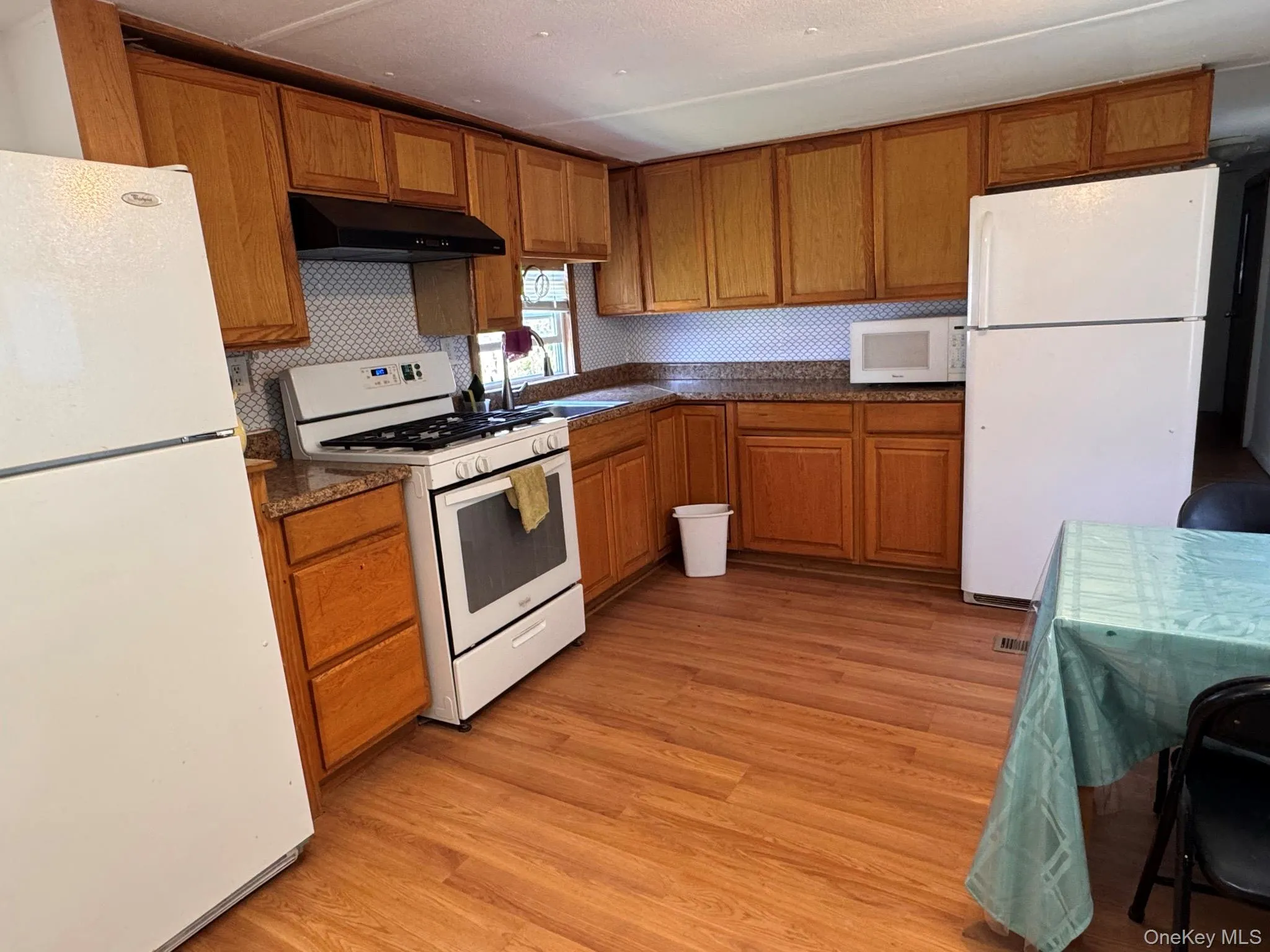 Kitchen featuring wood-finish flooring, oak cabinetry, granite-look countertops, and a white tile backsplash Kitchen featuring wood-finish flooring, oak cabinetry, granite-look countertops, and a white tile backsplash