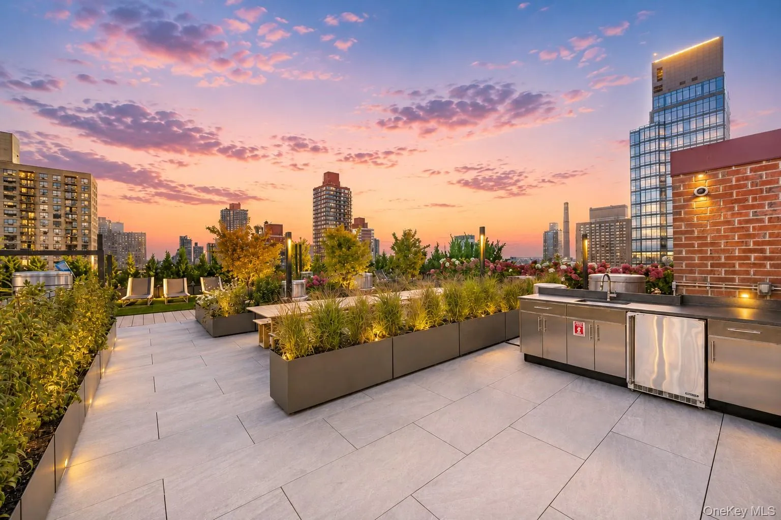 Rooftop terrace featuring light-toned paver flooring, extensive built-in planters with integrated lighting, and a brick accent wall Rooftop terrace featuring light-toned paver flooring, extensive built-in planters with integrated lighting, and a brick accent wall