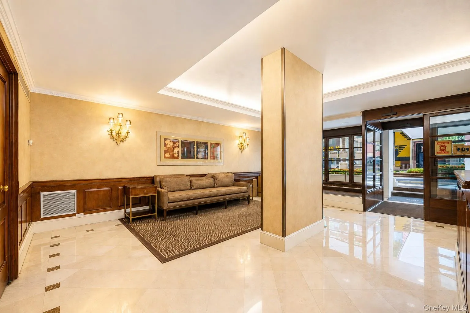Lobby entrance featuring polished marble flooring with inlay details, decorative wall sconces, wood paneling, and an illuminated recessed ceiling Lobby entrance featuring polished marble flooring with inlay details, decorative wall sconces, wood paneling, and an illuminated recessed ceiling