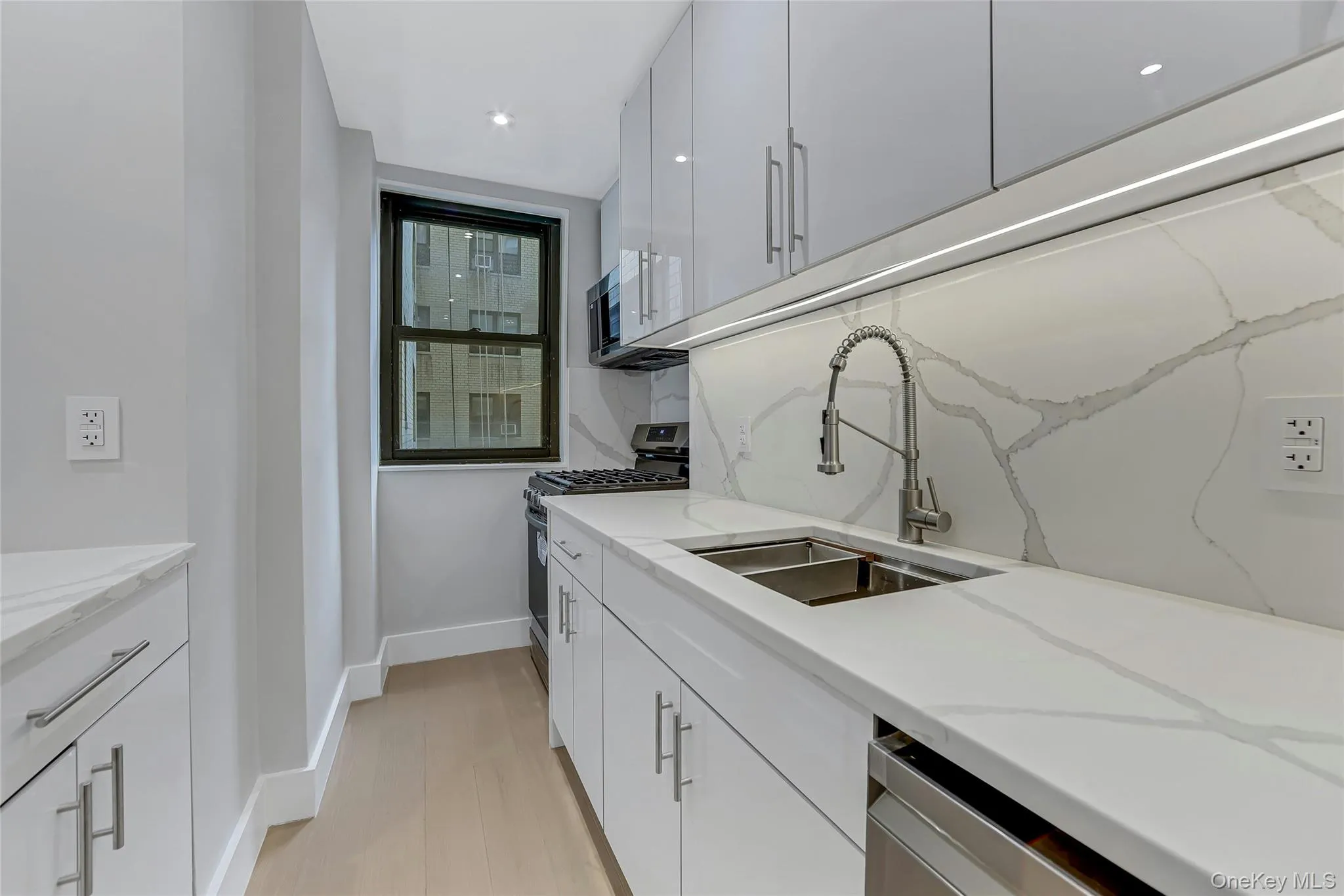 Galley kitchen featuring white cabinetry, light wood-finish flooring, a stainless steel double basin sink, light-toned countertops, and an integrated stainless steel dishwasher Galley kitchen featuring white cabinetry, light wood-finish flooring, a stainless steel double basin sink, light-toned countertops, and an integrated stainless steel dishwasher
