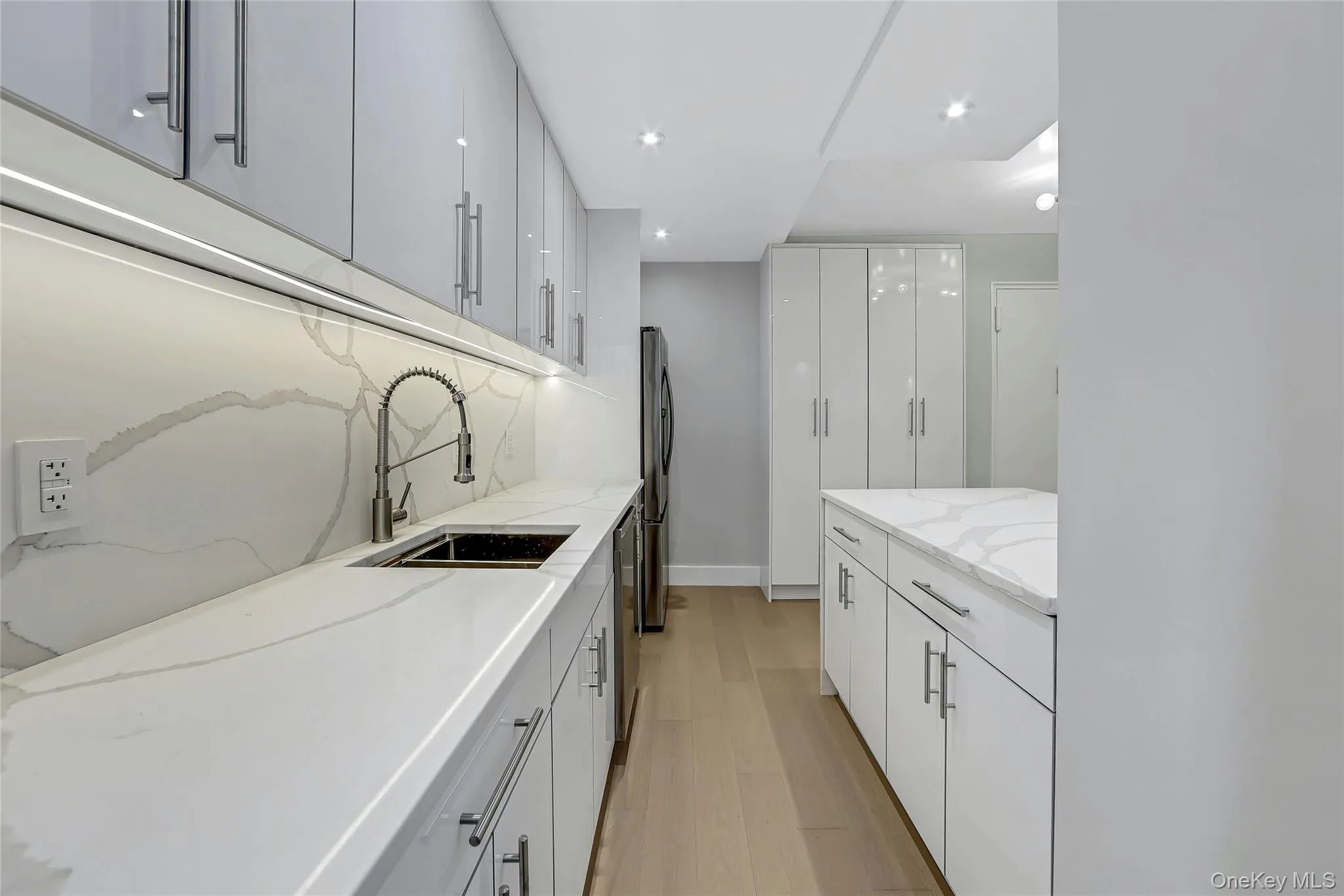 Galley kitchen featuring glossy white cabinetry, stainless steel appliances, and wood-finish flooring Galley kitchen featuring glossy white cabinetry, stainless steel appliances, and wood-finish flooring