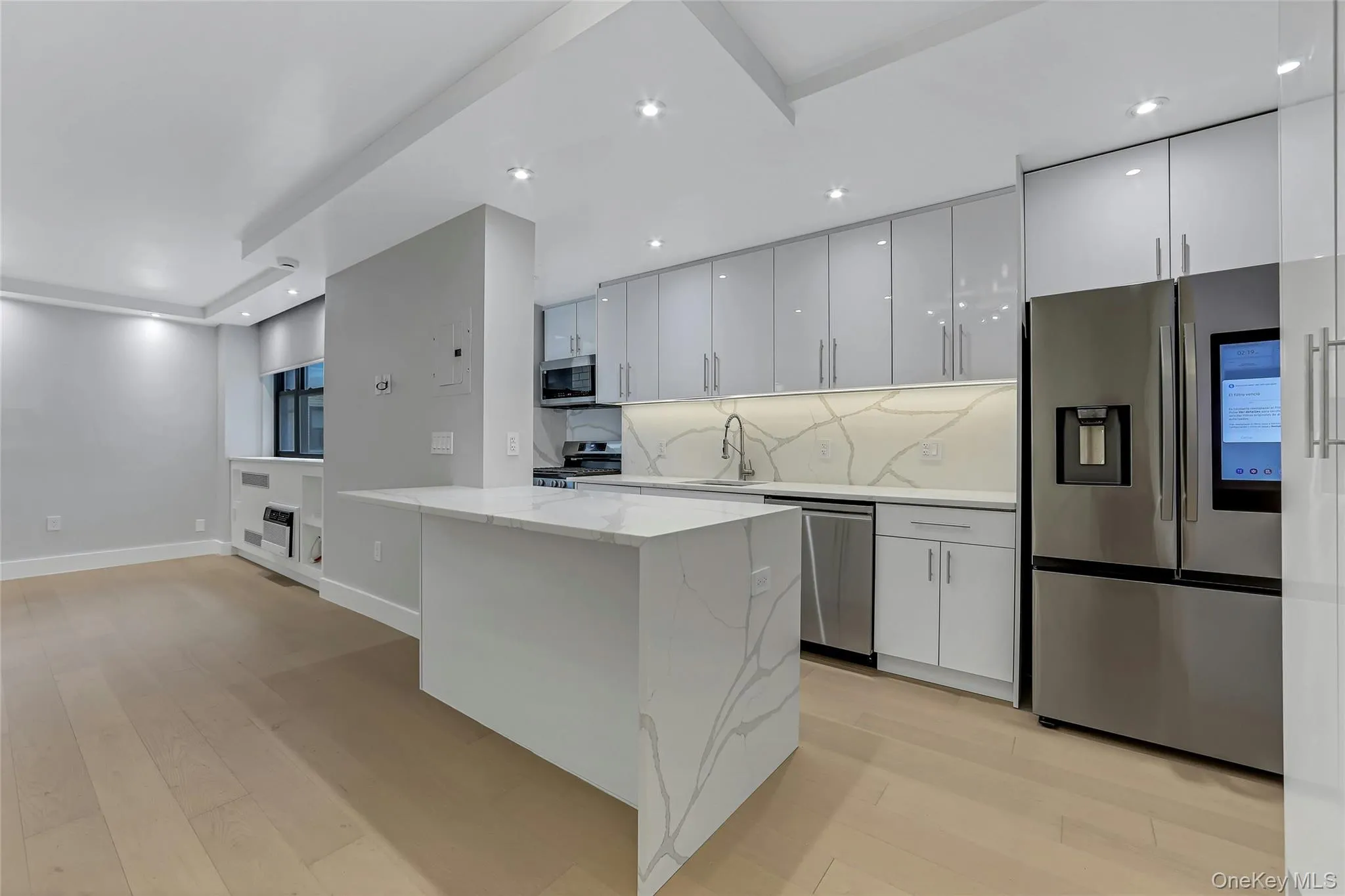 Contemporary kitchen featuring a waterfall island with a stone countertop, a matching stone backsplash, sleek gray cabinetry, stainless steel appliances, and light wood-finish flooring Contemporary kitchen featuring a waterfall island with a stone countertop, a matching stone backsplash, sleek gray cabinetry, stainless steel appliances, and light wood-finish flooring