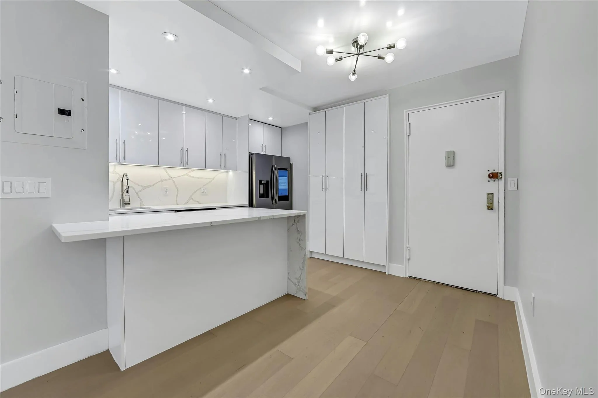 Modern kitchen featuring white high-gloss cabinetry, a white countertop with a waterfall edge, and a patterned backsplash Modern kitchen featuring white high-gloss cabinetry, a white countertop with a waterfall edge, and a patterned backsplash