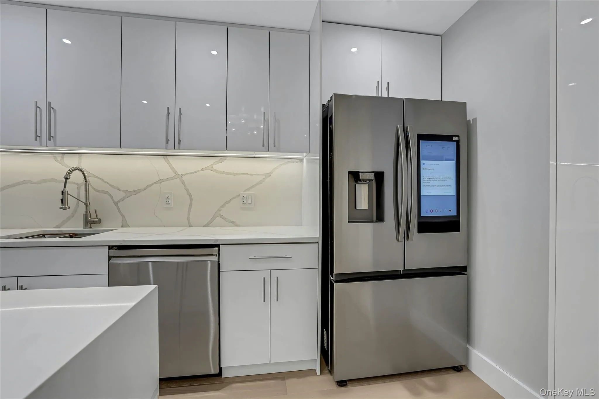 Contemporary kitchen featuring high-gloss white cabinetry, stainless steel appliances, a large stainless steel French door refrigerator with an integrated display, and a modern gooseneck faucet Contemporary kitchen featuring high-gloss white cabinetry, stainless steel appliances, a large stainless steel French door refrigerator with an integrated display, and a modern gooseneck faucet