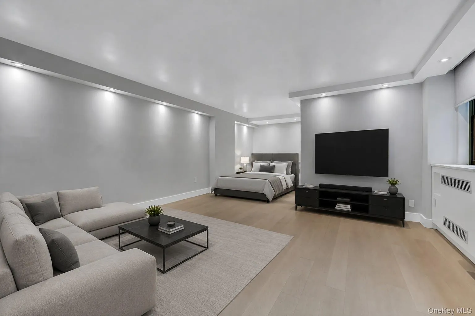 Open-concept living space with light wood-finish flooring, recessed lighting, a built-in window structure, and soft gray wall tones Open-concept living space with light wood-finish flooring, recessed lighting, a built-in window structure, and soft gray wall tones