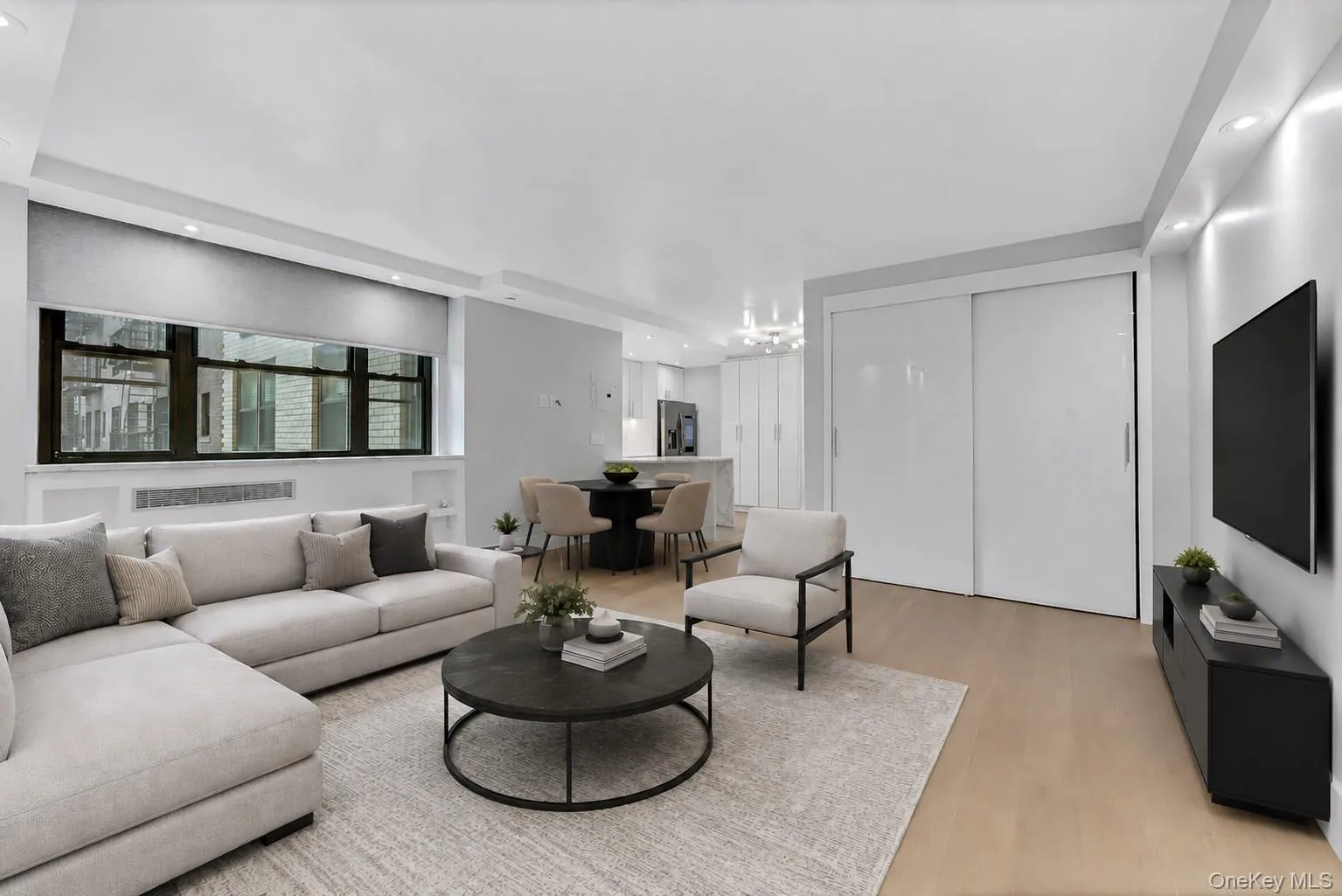 Expansive living area with wood-finish flooring, recessed lighting, and a large window featuring a built-in radiator cover Expansive living area with wood-finish flooring, recessed lighting, and a large window featuring a built-in radiator cover