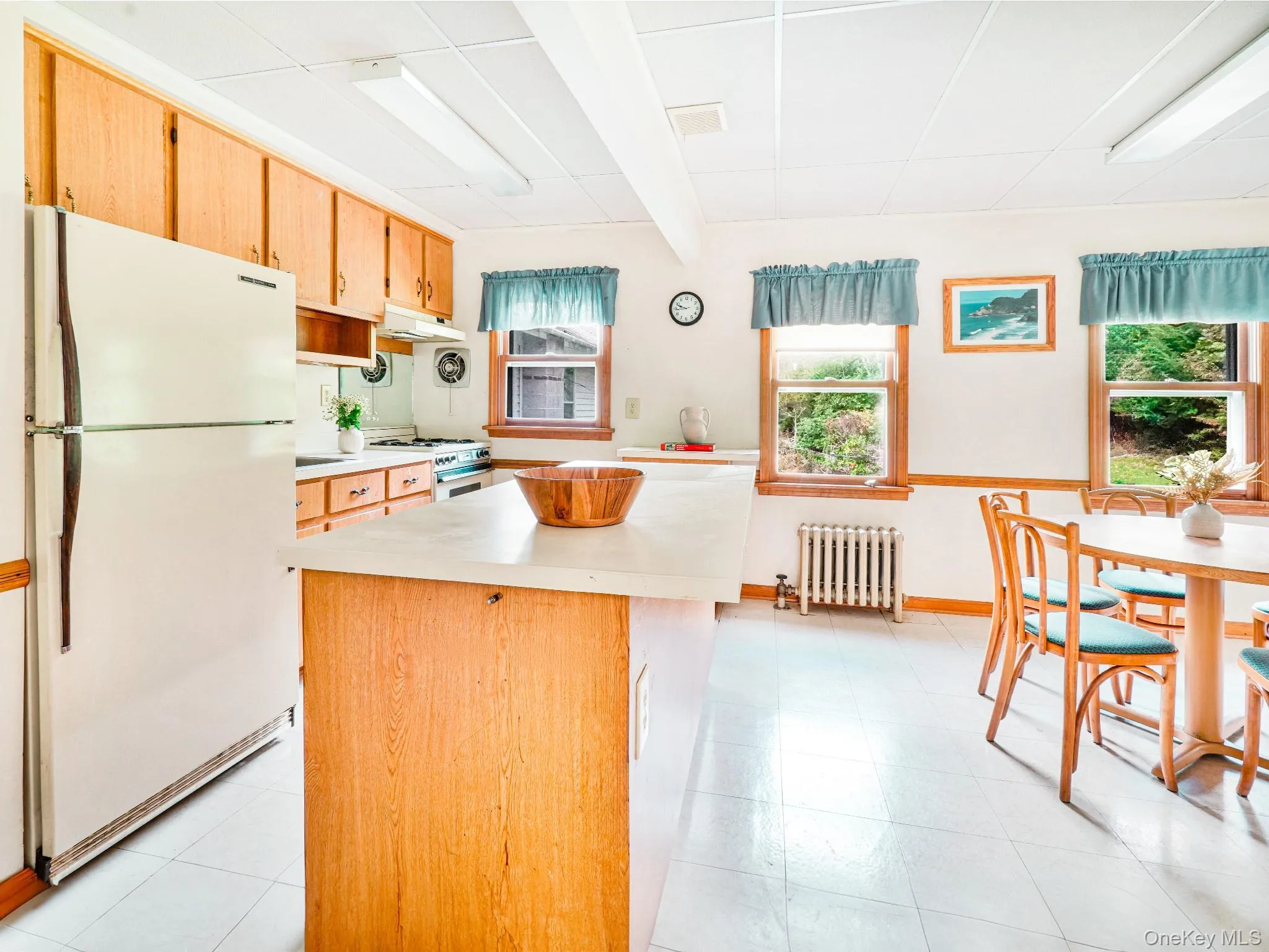 Kitchen with white appliances, radiator, light countertops, under cabinet range hood, and a kitchen island Kitchen with white appliances, radiator, light countertops, under cabinet range hood, and a kitchen island