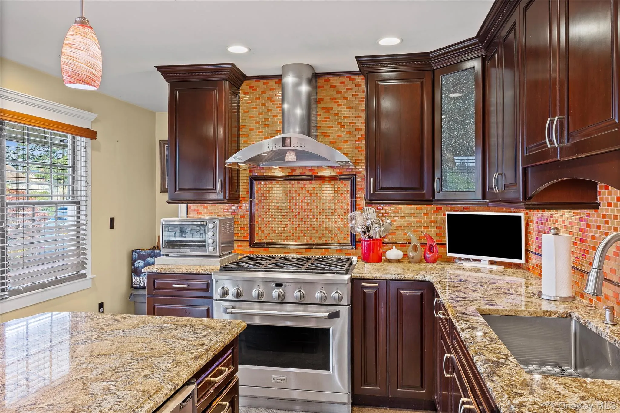 Kitchen with high end stainless steel range, wall chimney range hood, light stone countertops, decorative backsplash, and dark brown cabinetry Kitchen with high end stainless steel range, wall chimney range hood, light stone countertops, decorative backsplash, and dark brown cabinetry