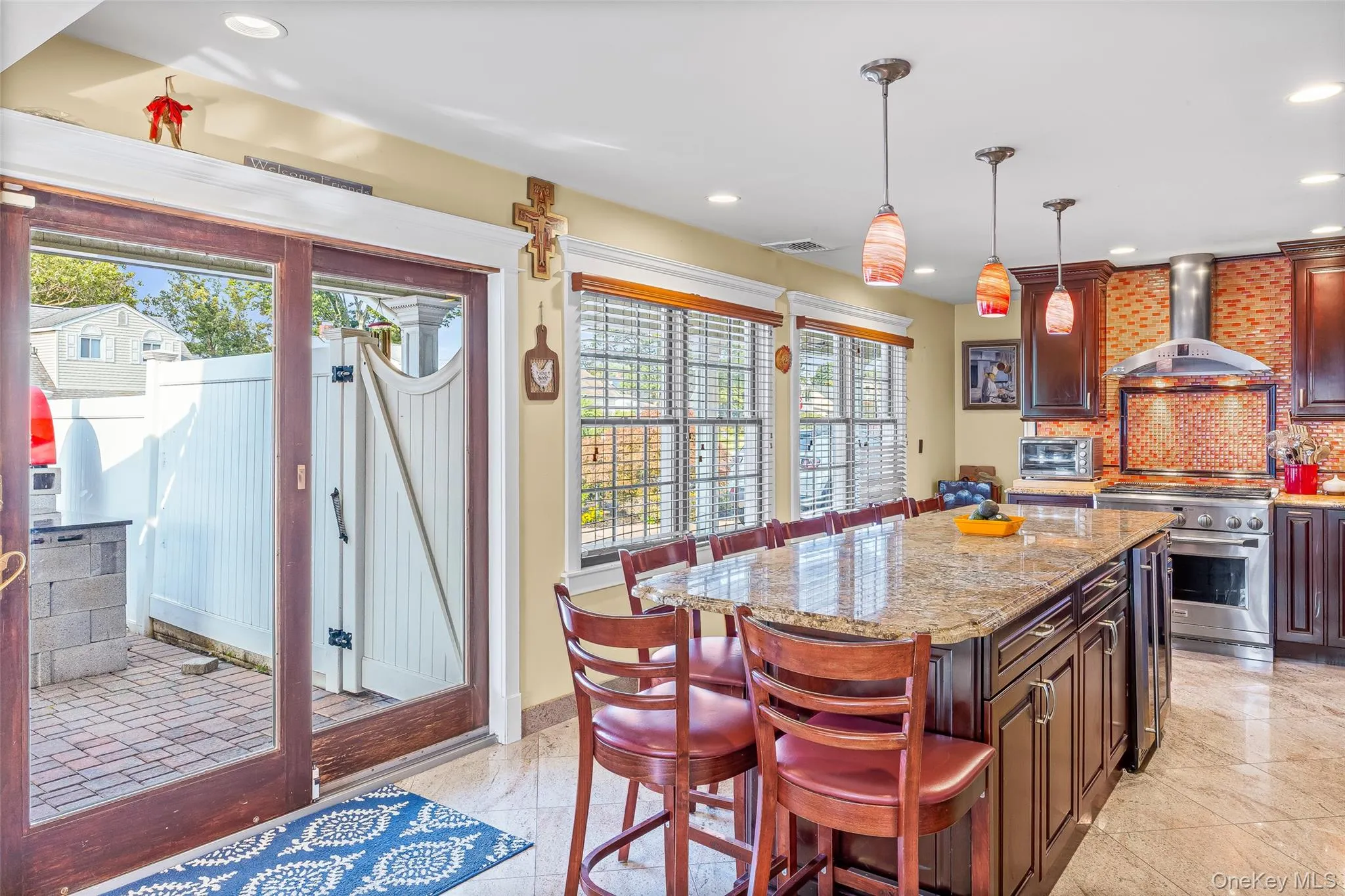 Kitchen with a breakfast bar, decorative backsplash, light stone counters, hanging light fixtures, and wall chimney exhaust hood Kitchen with a breakfast bar, decorative backsplash, light stone counters, hanging light fixtures, and wall chimney exhaust hood