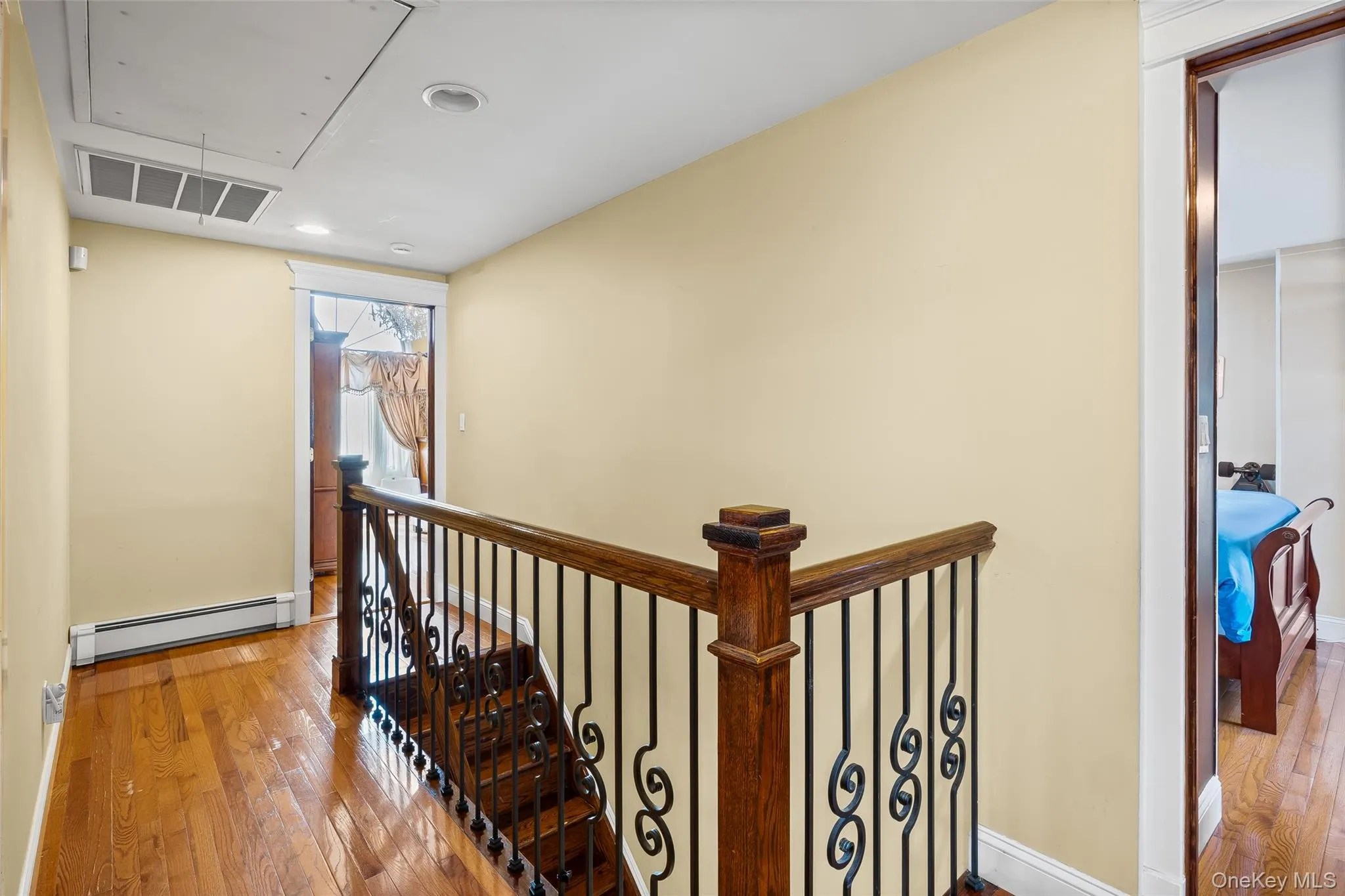 Stairway featuring attic access, wood-type flooring, and a baseboard heating unit Stairway featuring attic access, wood-type flooring, and a baseboard heating unit