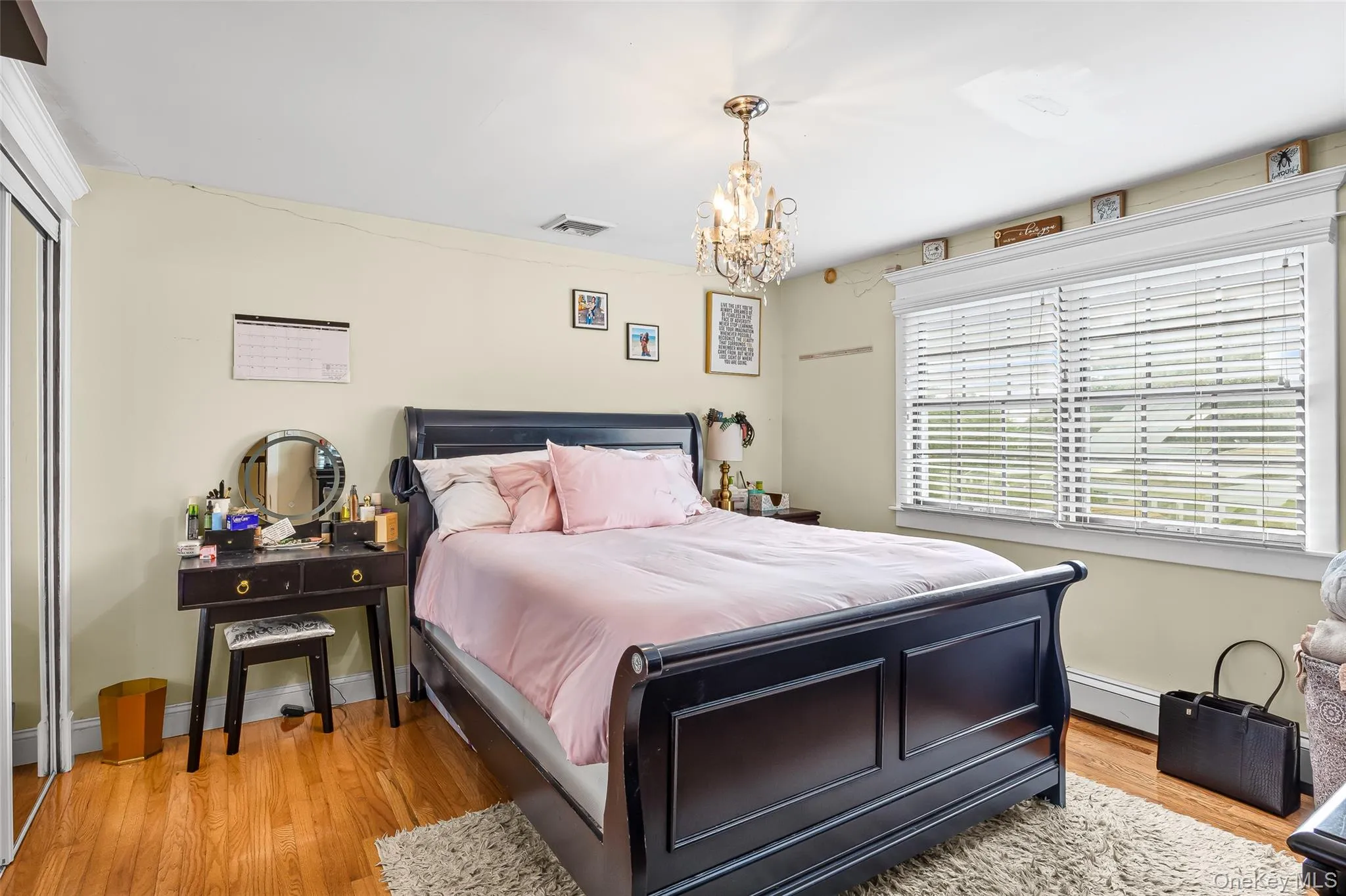 Bedroom featuring light wood-style floors, baseboard heating, a chandelier, and a closet Bedroom featuring light wood-style floors, baseboard heating, a chandelier, and a closet