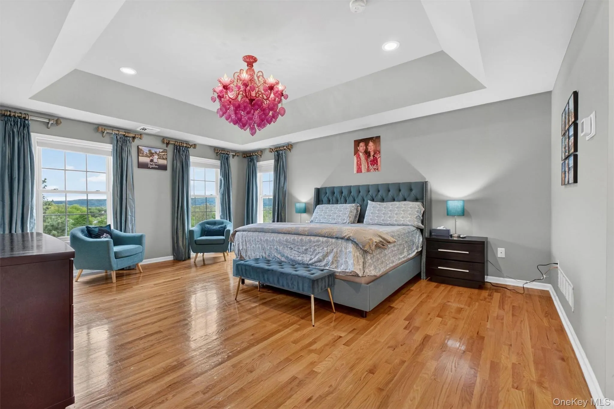 Expansive primary suite with tray ceiling, hardwood floors, sitting area, and scenic views. Expansive primary suite with tray ceiling, hardwood floors, sitting area, and scenic views.