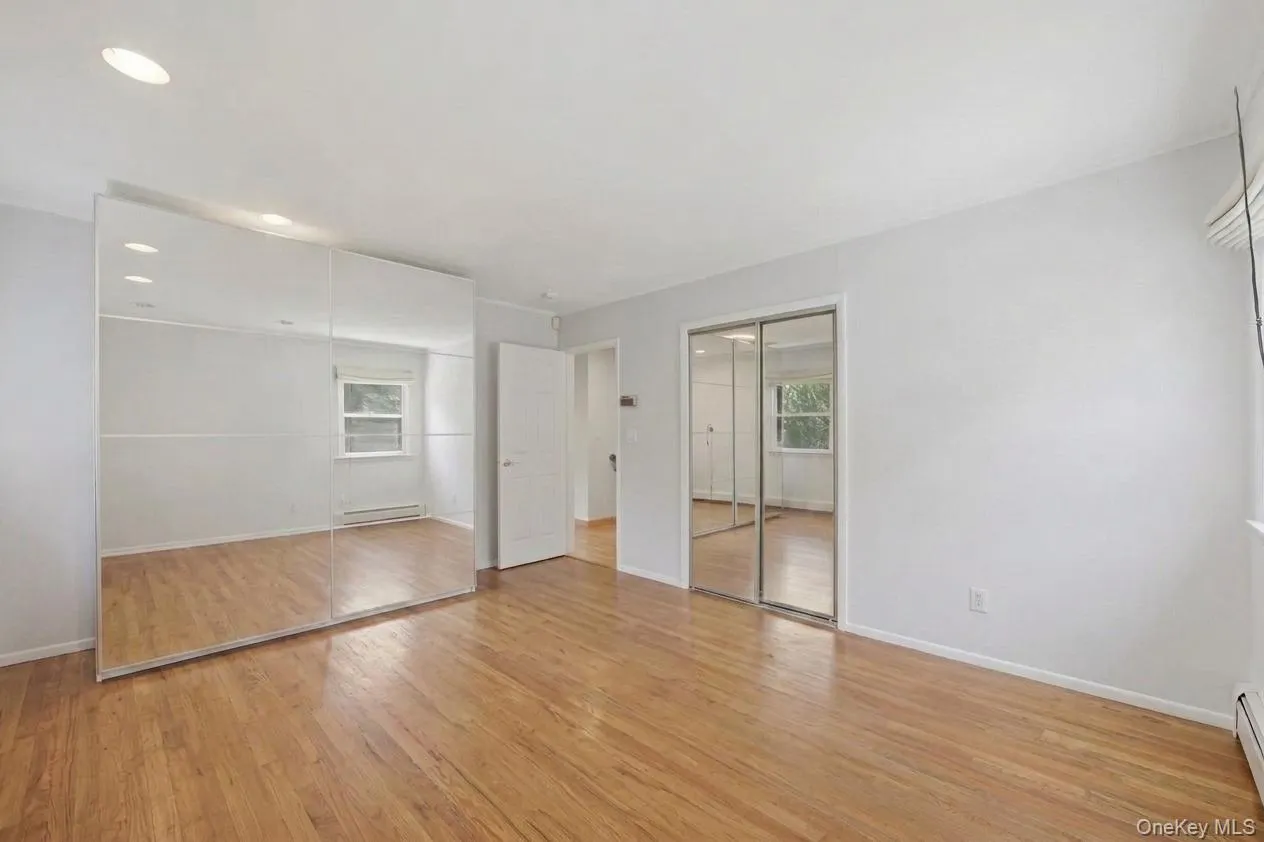 Primary bedroom with hardwood flooring throughout featuring recessed lighting and mirrored closet doors Primary bedroom with hardwood flooring throughout featuring recessed lighting and mirrored closet doors