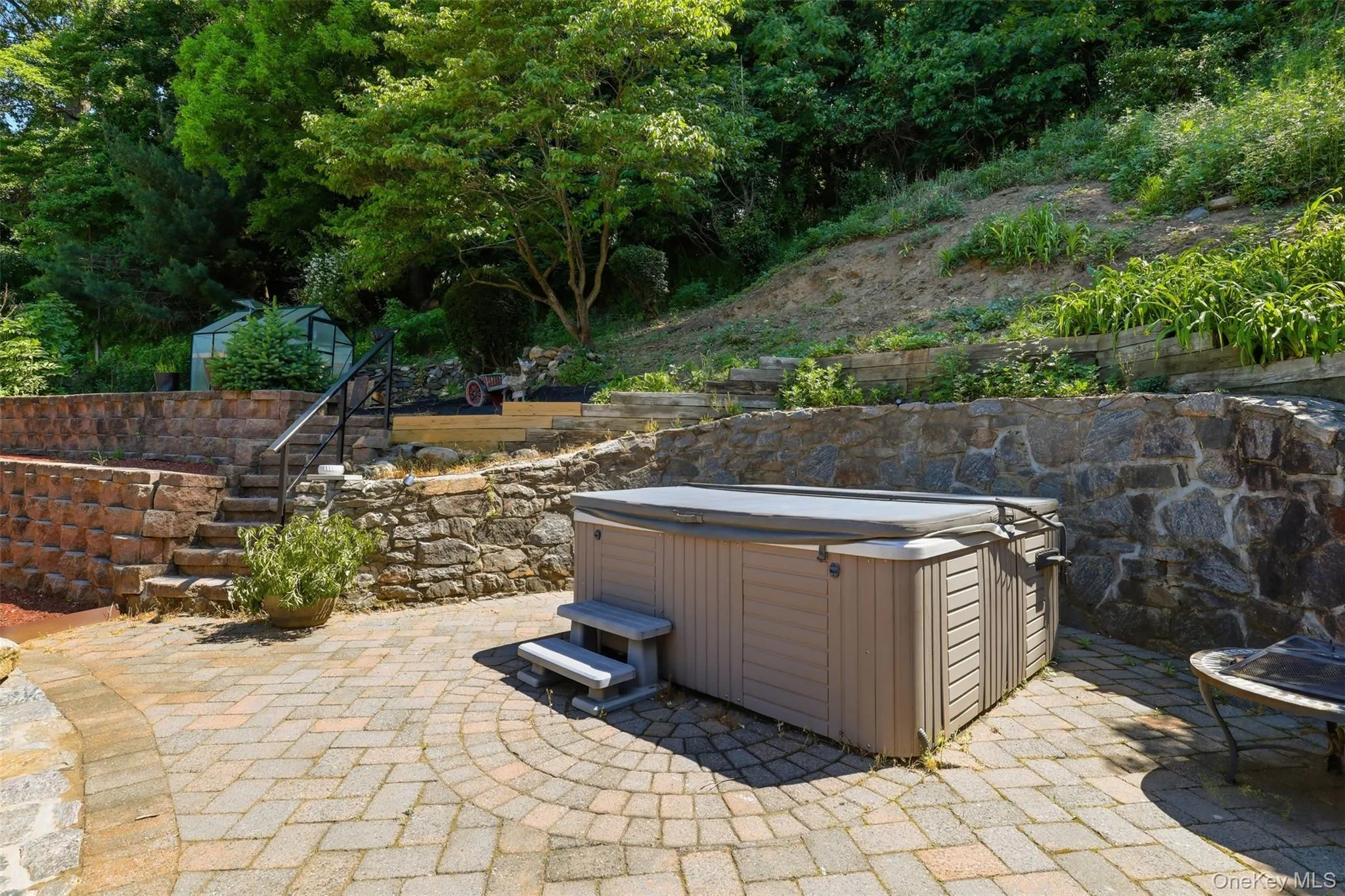 Outdoor patio featuring a hot tub with cover, stone retaining walls, and paver flooring Outdoor patio featuring a hot tub with cover, stone retaining walls, and paver flooring