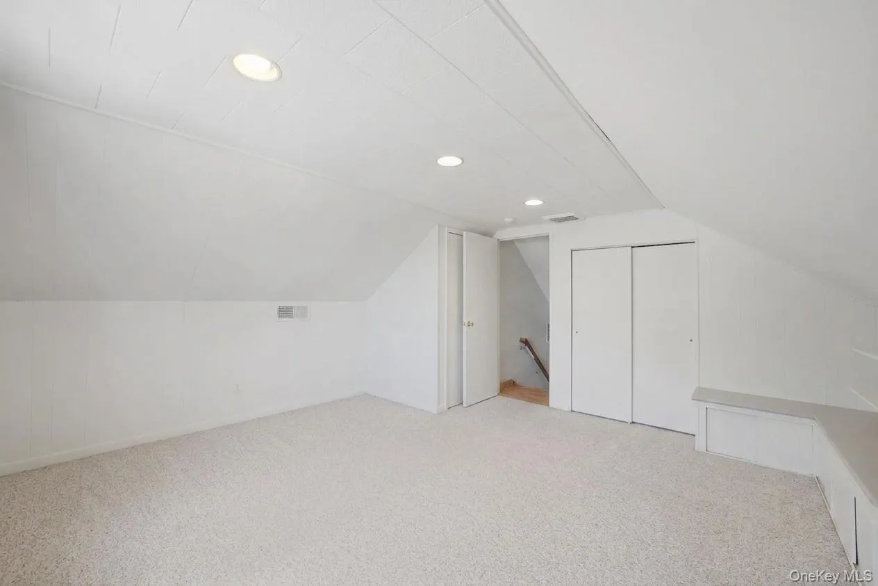 Spacious attic bedroom featuring sloped ceilings, recessed lighting, neutral carpeting, plenty of closet space, and built-in storage benches Spacious attic bedroom featuring sloped ceilings, recessed lighting, neutral carpeting, plenty of closet space, and built-in storage benches