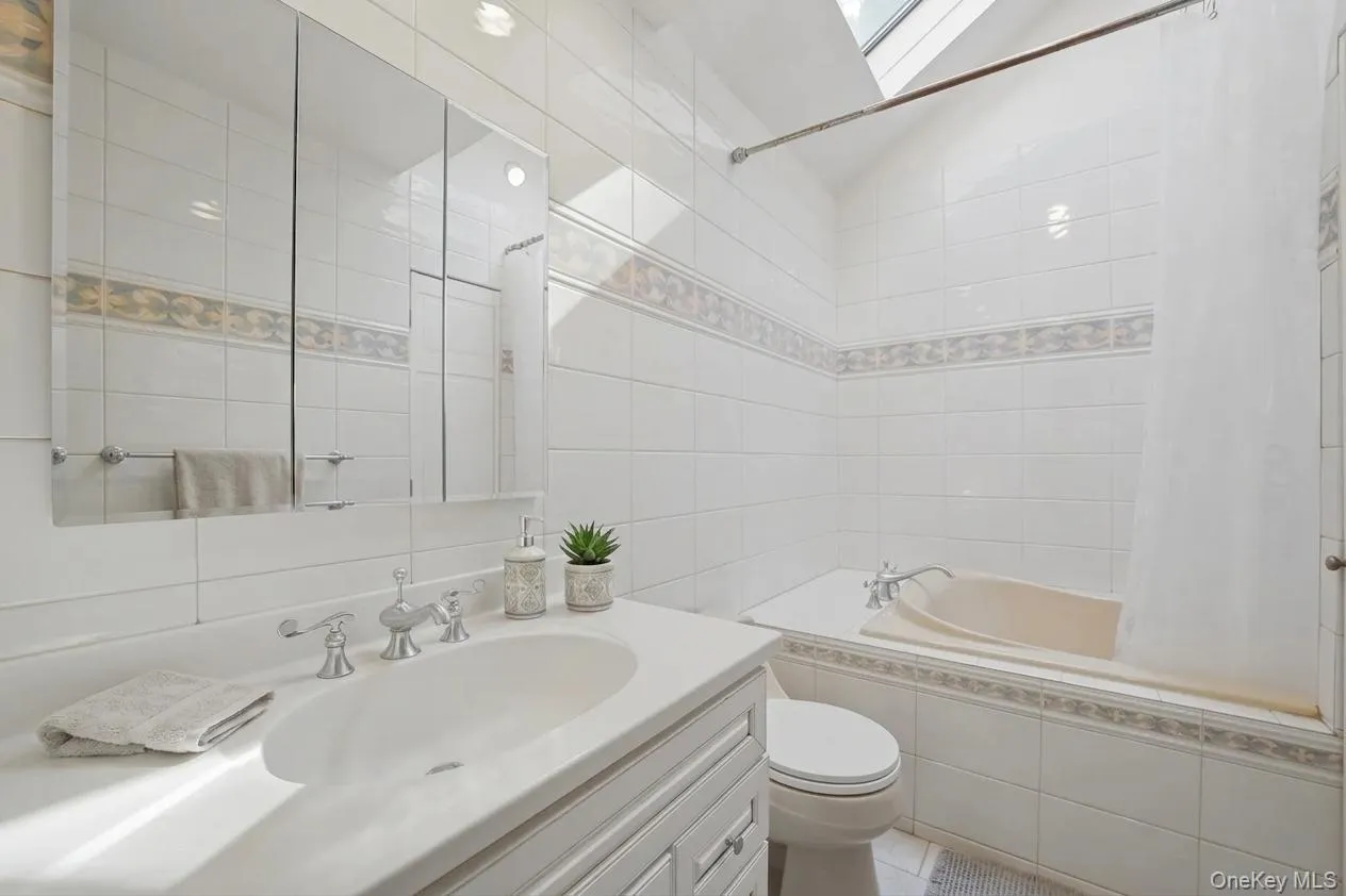 2nd floor bathroom featuring a white tile surround, decorative accent tile band, white vanity with integrated sink, chrome faucet, and mirrored medicine cabinet 2nd floor bathroom featuring a white tile surround, decorative accent tile band, white vanity with integrated sink, chrome faucet, and mirrored medicine cabinet