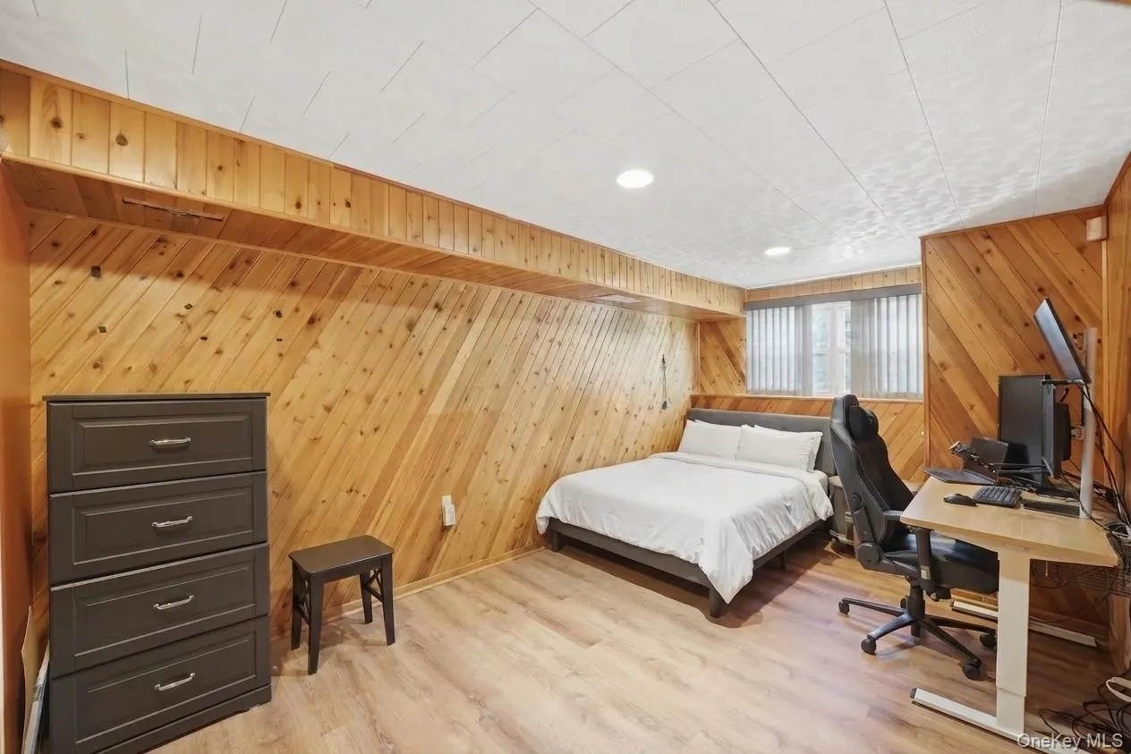 Basement bedroom featuring wood-finish flooring, diagonal wood paneling, recessed lighting, and a white ceiling with a textured finish Basement bedroom featuring wood-finish flooring, diagonal wood paneling, recessed lighting, and a white ceiling with a textured finish