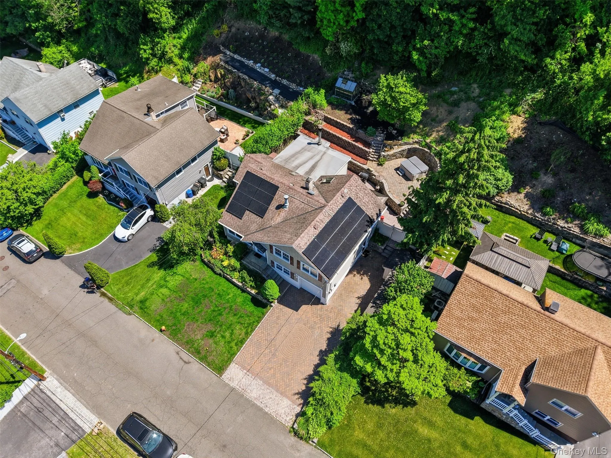 Property featuring solar panels, a multi-level terraced backyard, mature trees, a paved driveway, and manicured lawns Property featuring solar panels, a multi-level terraced backyard, mature trees, a paved driveway, and manicured lawns
