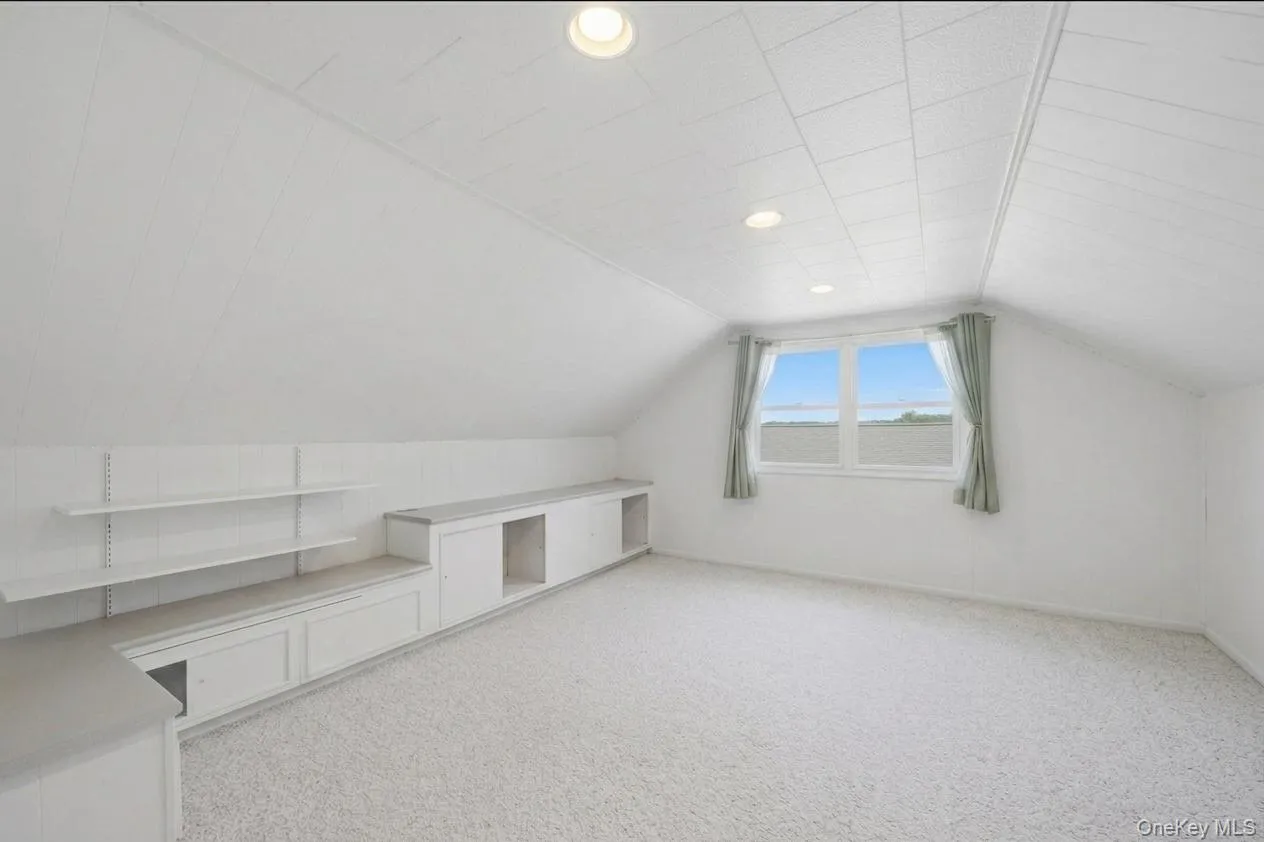 Bright attic bedroom featuring light-toned carpeting, a window with distant scenery, and recessed lighting Bright attic bedroom featuring light-toned carpeting, a window with distant scenery, and recessed lighting