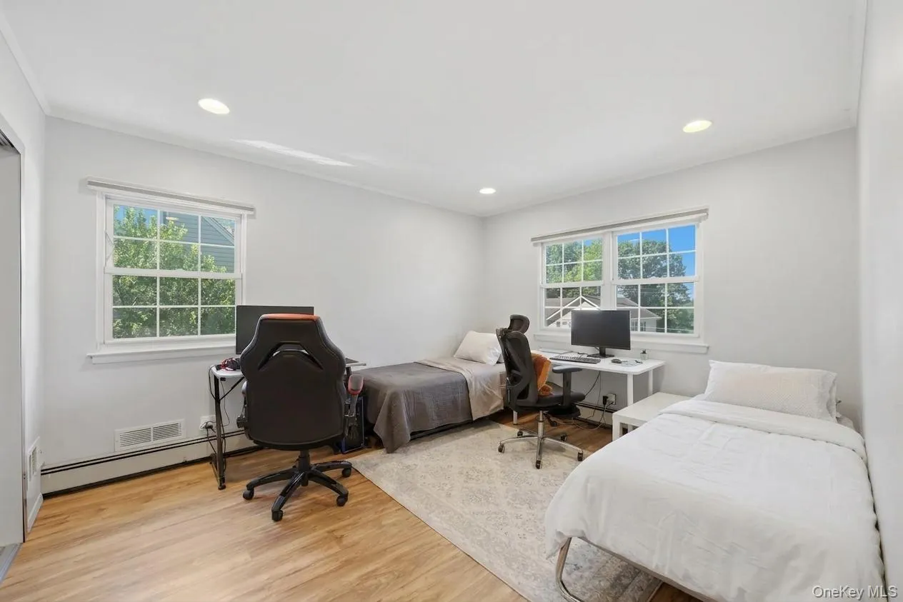 Bright 2nd bedroom featuring wood-finish flooring, recessed lighting, and two windows with white trim Bright 2nd bedroom featuring wood-finish flooring, recessed lighting, and two windows with white trim