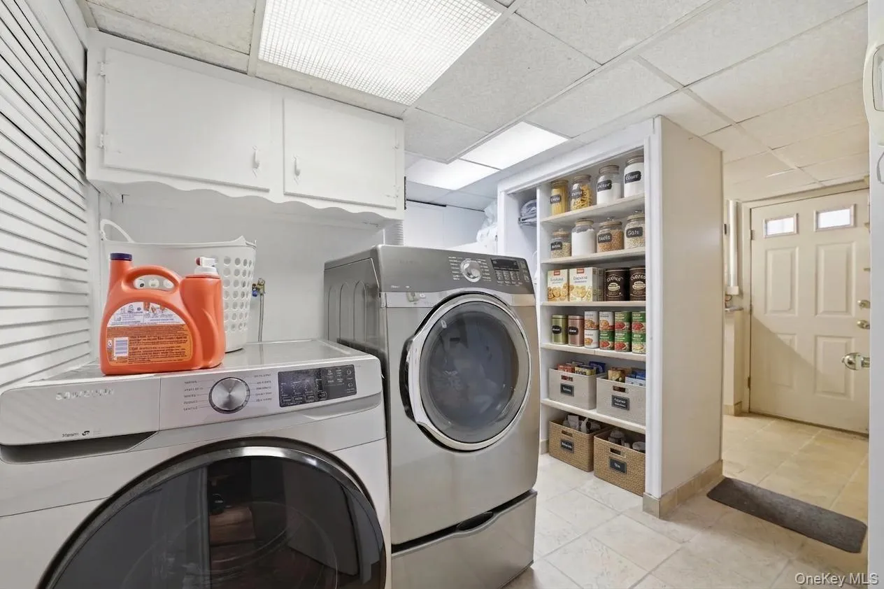 Dedicated laundry area in basement featuring white upper cabinetry, built-in shelving, and tile flooring Dedicated laundry area in basement featuring white upper cabinetry, built-in shelving, and tile flooring