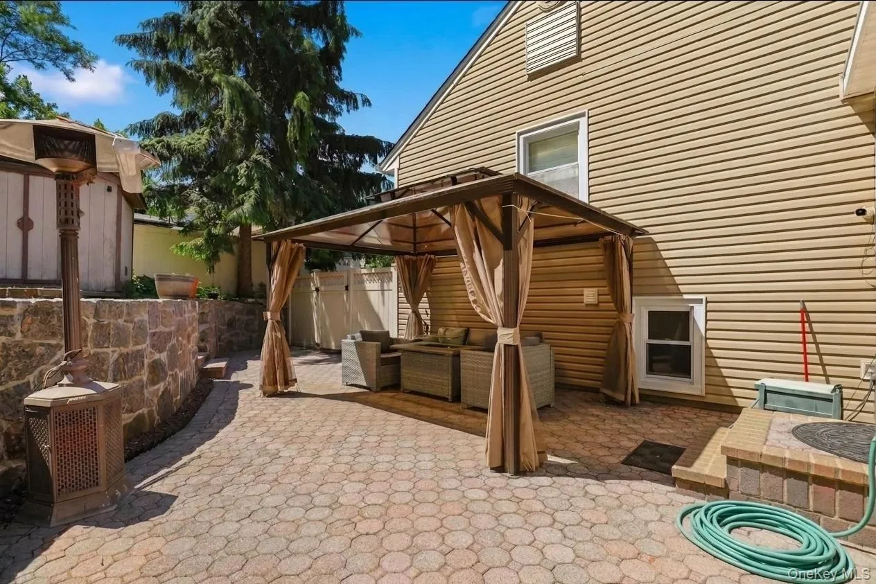 Paved patio area featuring a covered gazebo structure, stone retaining walls, and a large mature tree Paved patio area featuring a covered gazebo structure, stone retaining walls, and a large mature tree