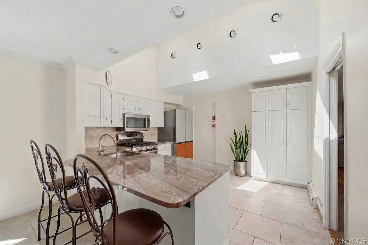 Kitchen featuring a large island with stone countertop, stainless steel appliances, white cabinetry, sky light, and recessed lighting Kitchen featuring a large island with stone countertop, stainless steel appliances, white cabinetry, sky light, and recessed lighting