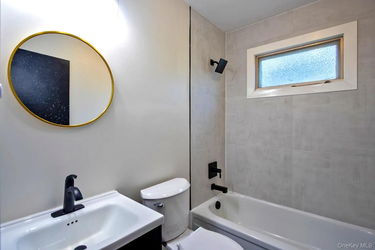 Bathroom featuring a white bathtub, light-toned wall tile, and a frosted window Bathroom featuring a white bathtub, light-toned wall tile, and a frosted window