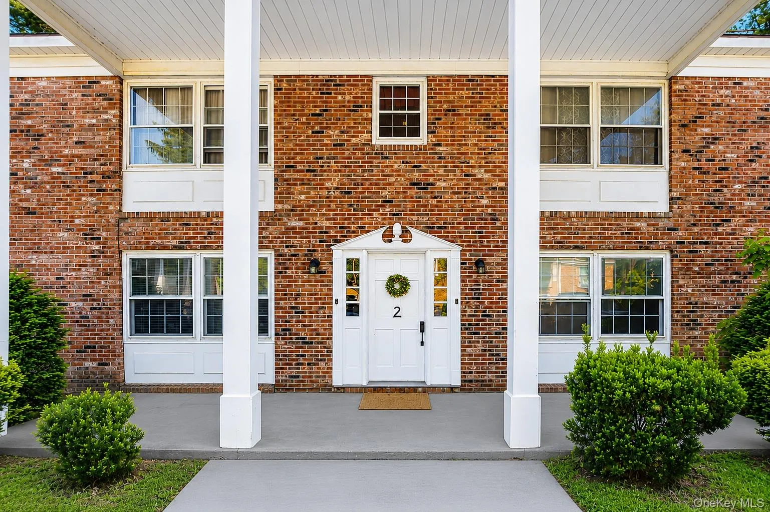 Brick exterior featuring white column accents, a covered entry, decorative front door sidelights, and established landscaping Brick exterior featuring white column accents, a covered entry, decorative front door sidelights, and established landscaping