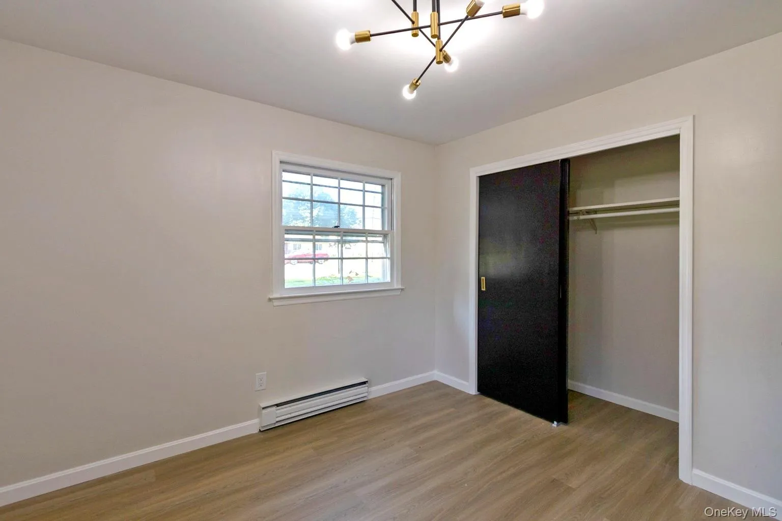 Neutral-toned room with wood-finish flooring, a modern sputnik-style ceiling light fixture, and a window with white trim Neutral-toned room with wood-finish flooring, a modern sputnik-style ceiling light fixture, and a window with white trim