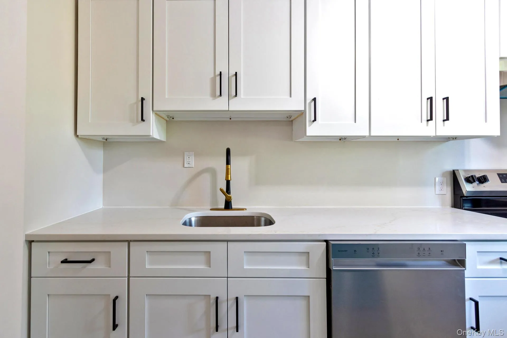 White shaker-style cabinetry with matte black hardware, stainless steel undermount sink with a two-tone faucet, solid surface countertop, and stainless steel dishwasher White shaker-style cabinetry with matte black hardware, stainless steel undermount sink with a two-tone faucet, solid surface countertop, and stainless steel dishwasher
