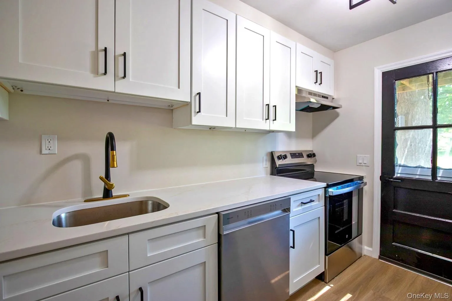 Kitchen featuring white shaker-style cabinetry, light-toned countertops, stainless steel appliances, and wood-finish flooring Kitchen featuring white shaker-style cabinetry, light-toned countertops, stainless steel appliances, and wood-finish flooring