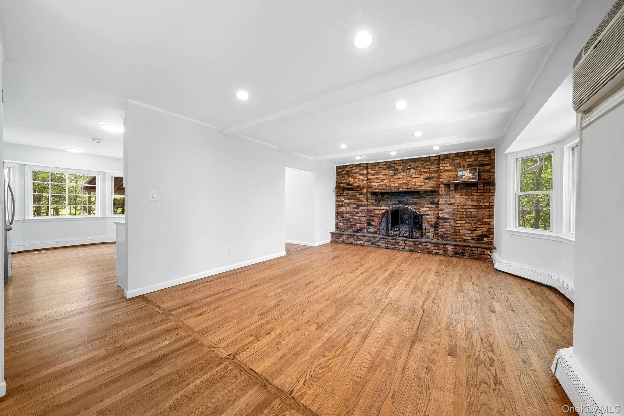 Spacious living area featuring a prominent brick fireplace with a stone hearth, recessed lighting, wood-finish flooring, and a bay window Spacious living area featuring a prominent brick fireplace with a stone hearth, recessed lighting, wood-finish flooring, and a bay window