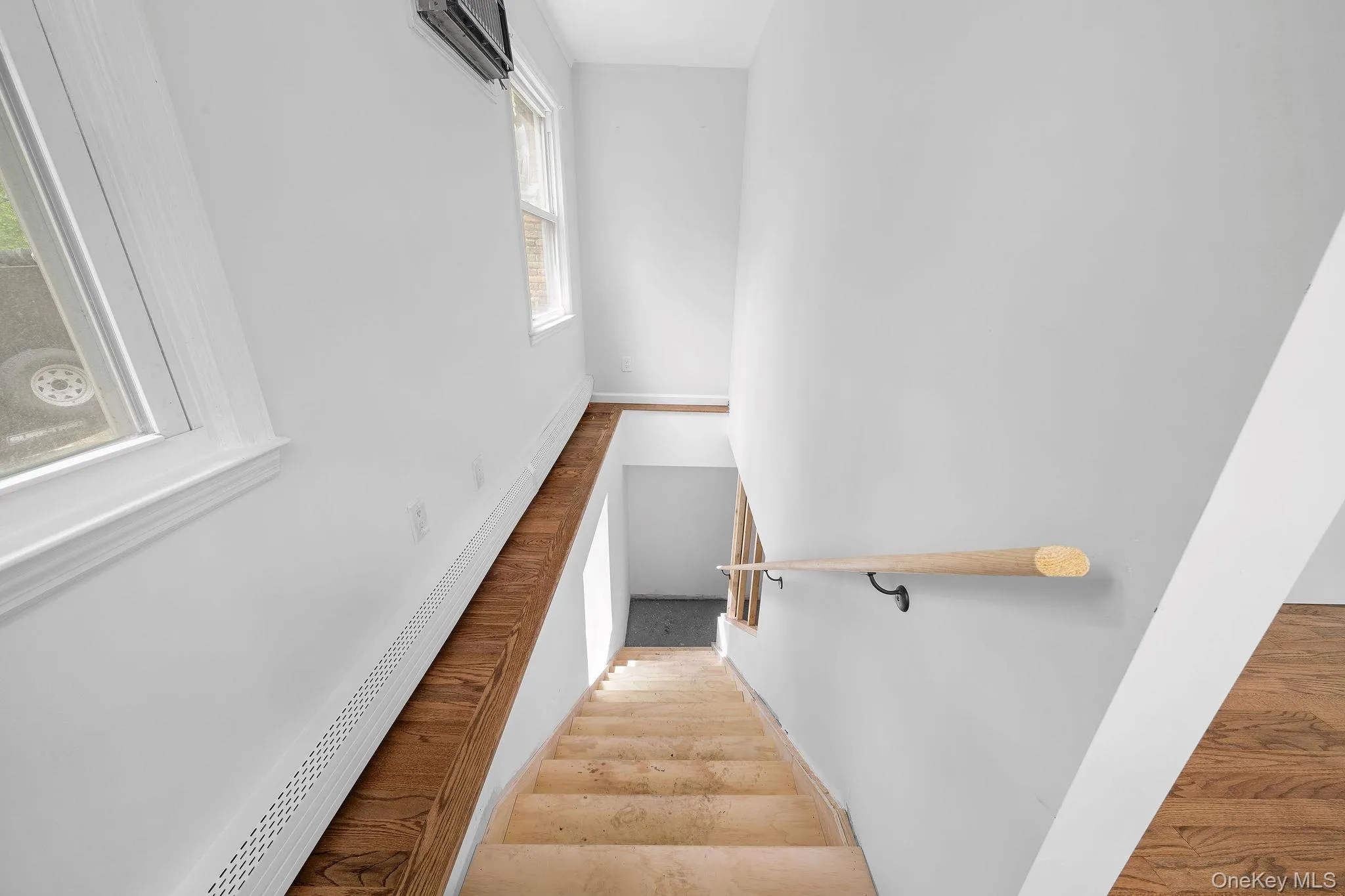 Staircase with light wood-finish treads and risers, complemented by a natural wood-finish handrail with black mounts Staircase with light wood-finish treads and risers, complemented by a natural wood-finish handrail with black mounts