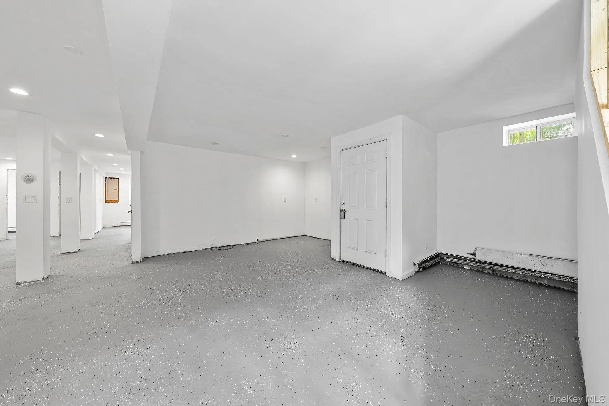Expansive room featuring painted concrete flooring, recessed lighting, and white walls Expansive room featuring painted concrete flooring, recessed lighting, and white walls